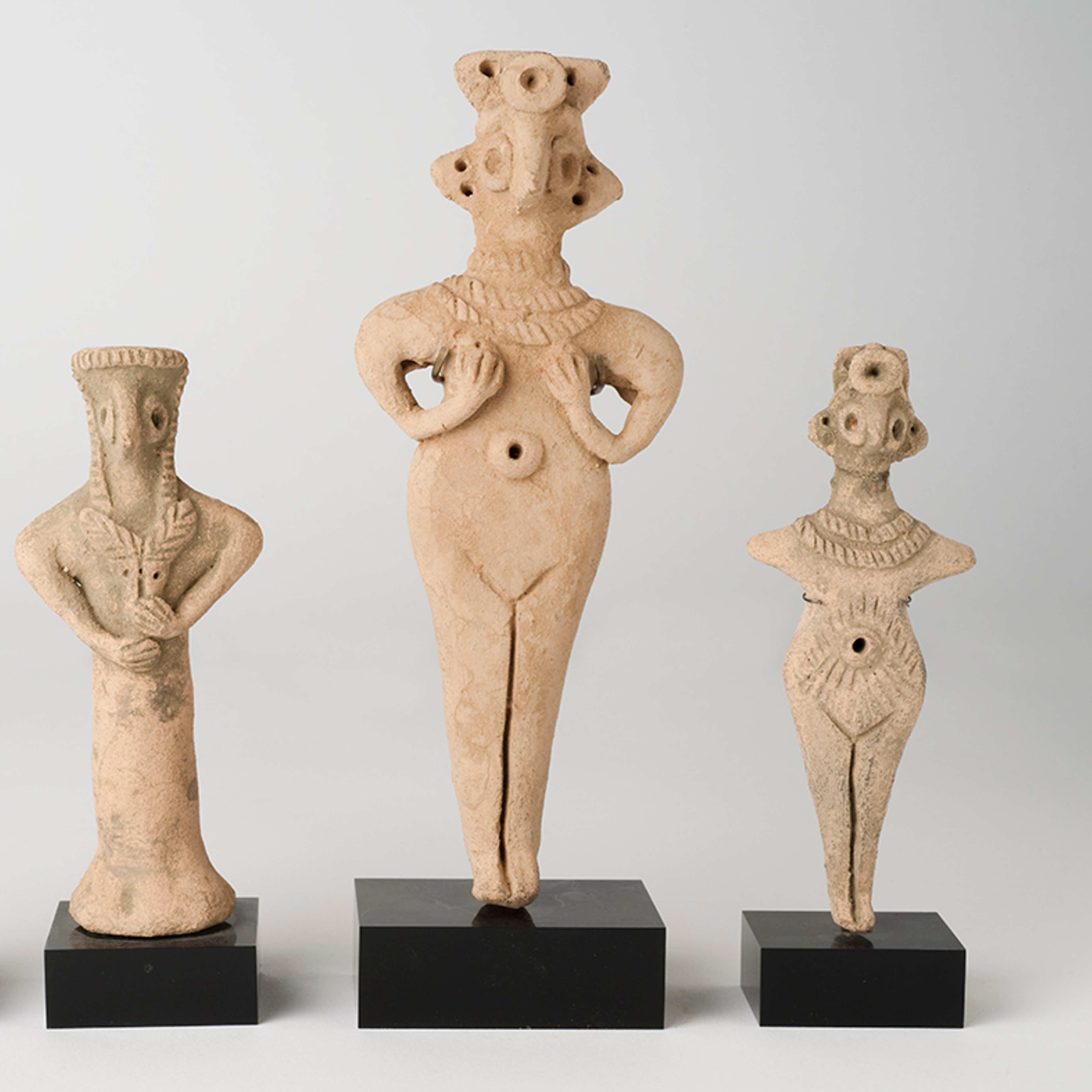 Four terracotta figurines of semi-abstracted human shapes in a row