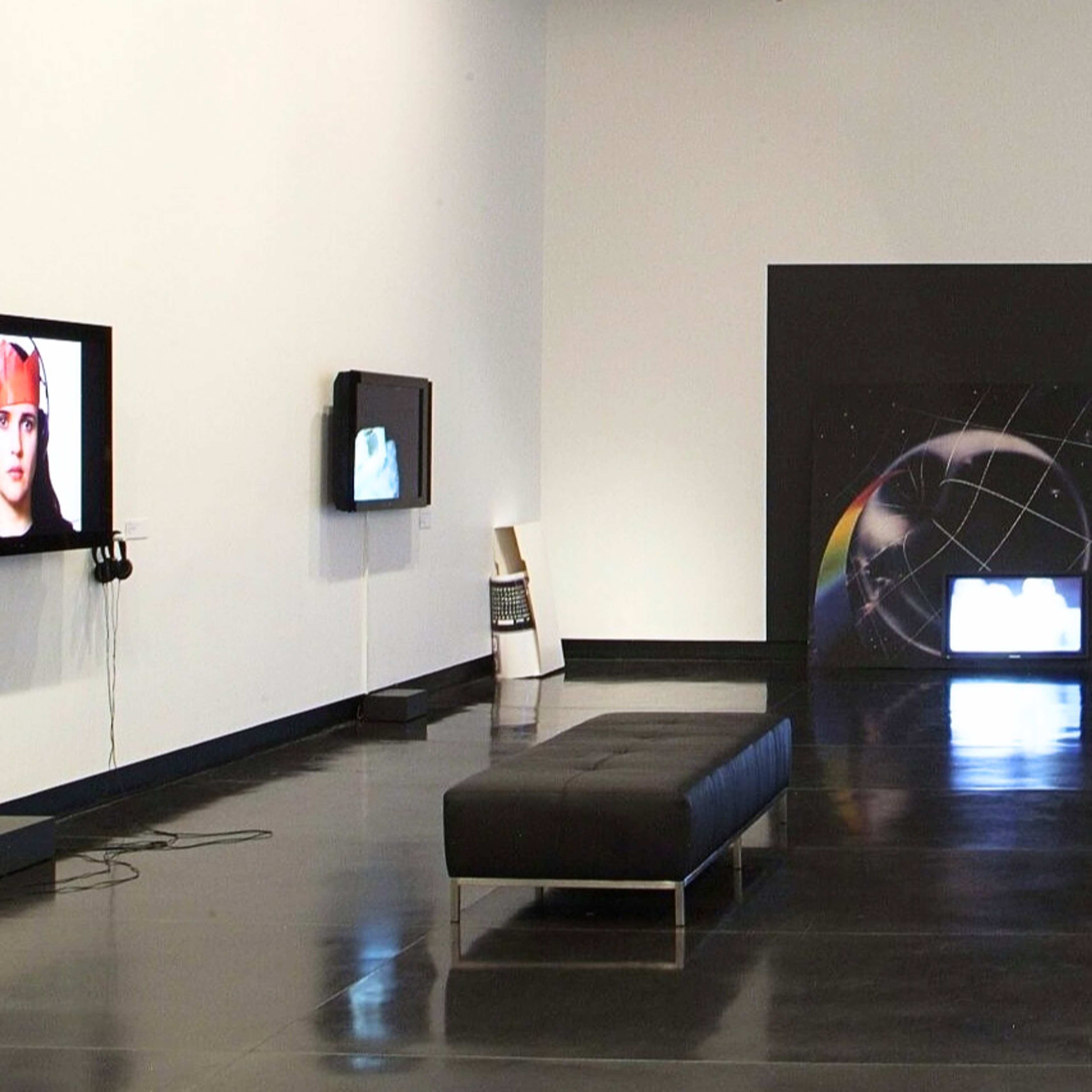 A photograph of a gallery space with several screens and paintings on the wall