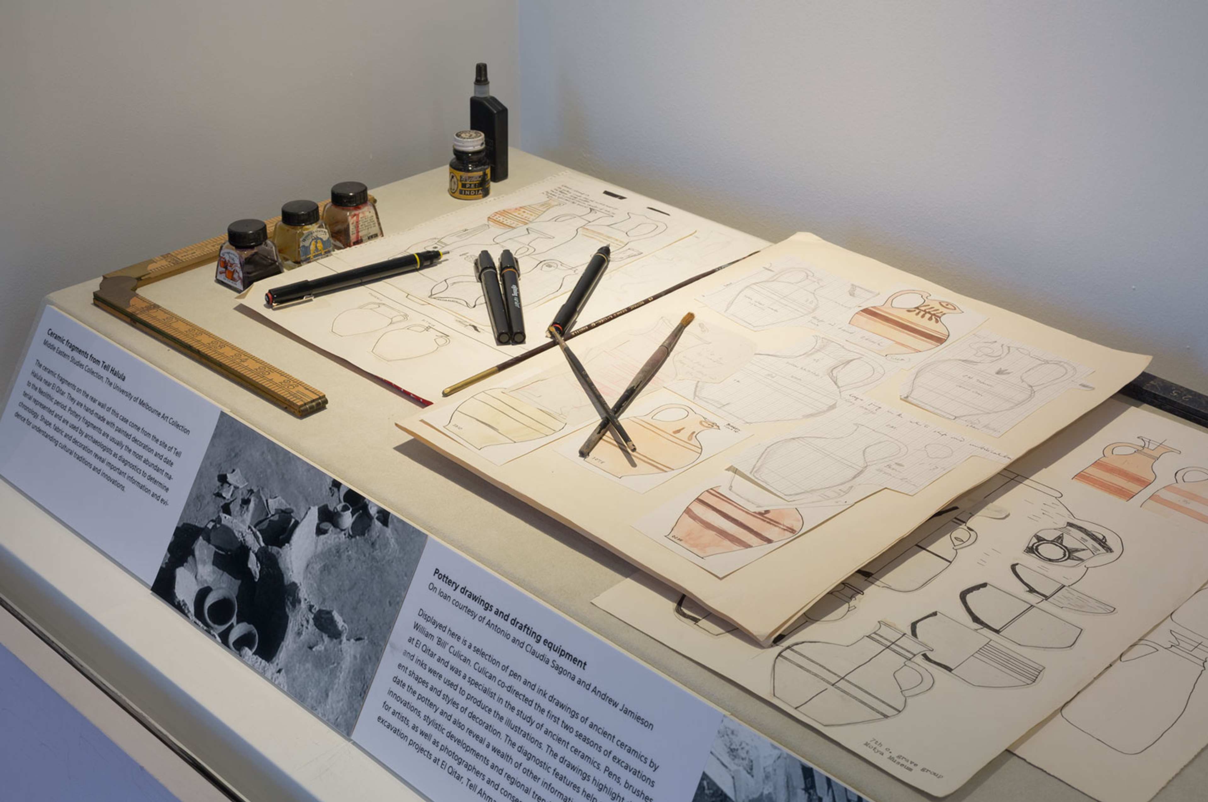 Drawings of pottery and drawing implements displayed in a museum cabinet