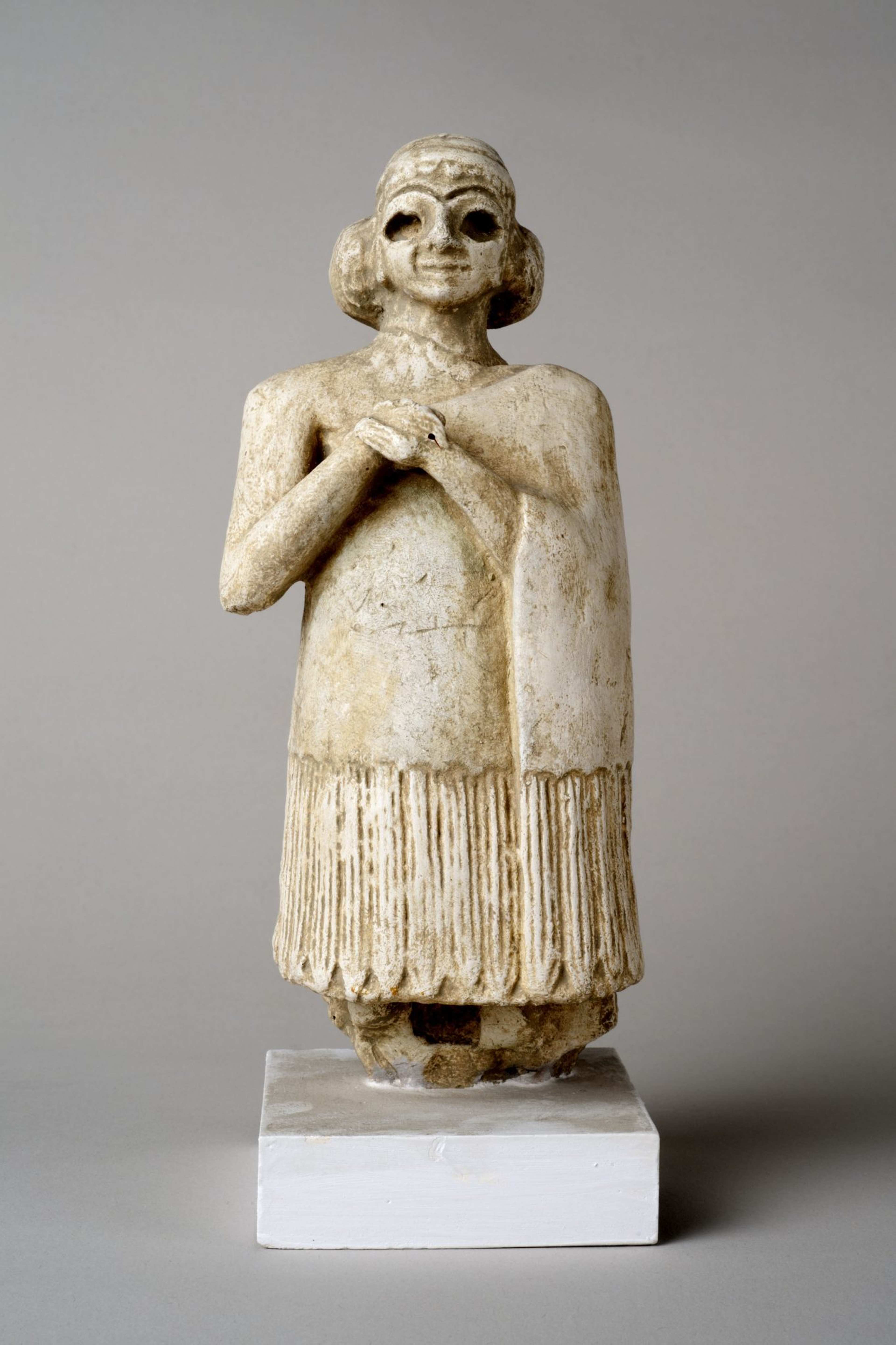 A photograph of an ancient figurine in a long coat and arms folded at chest