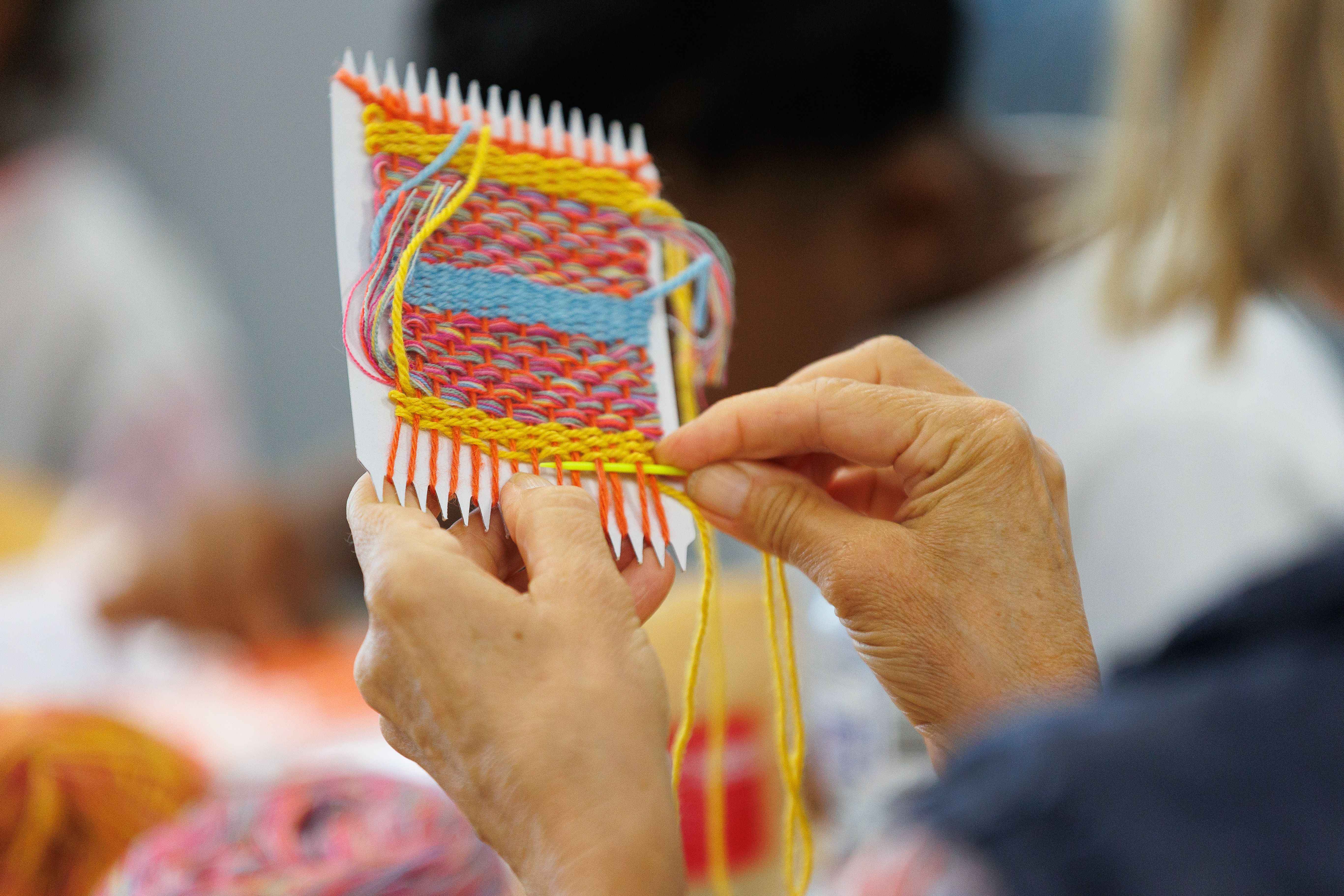 A close up of a person doing a colourful weaving.