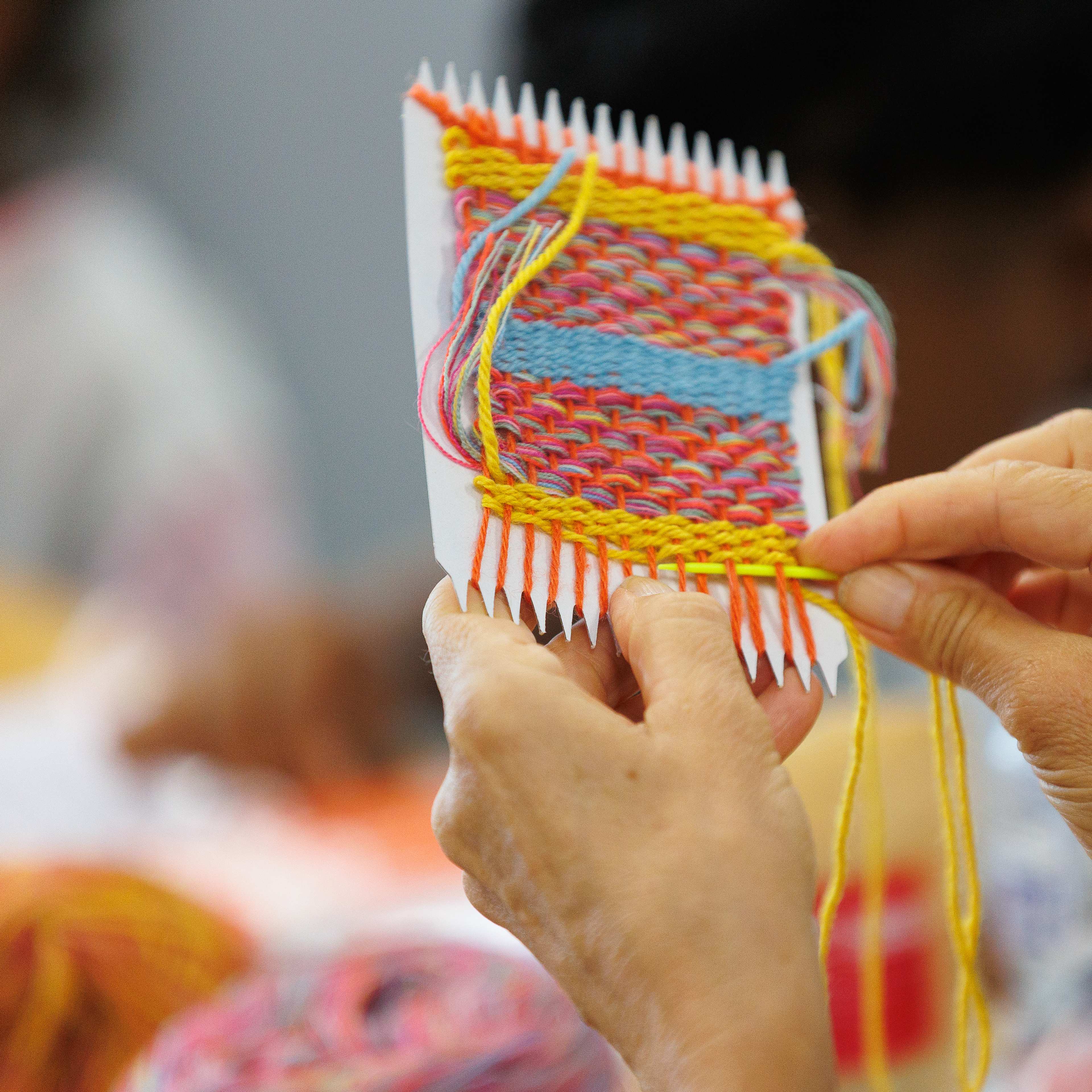 A close up of a person doing a colourful weaving.