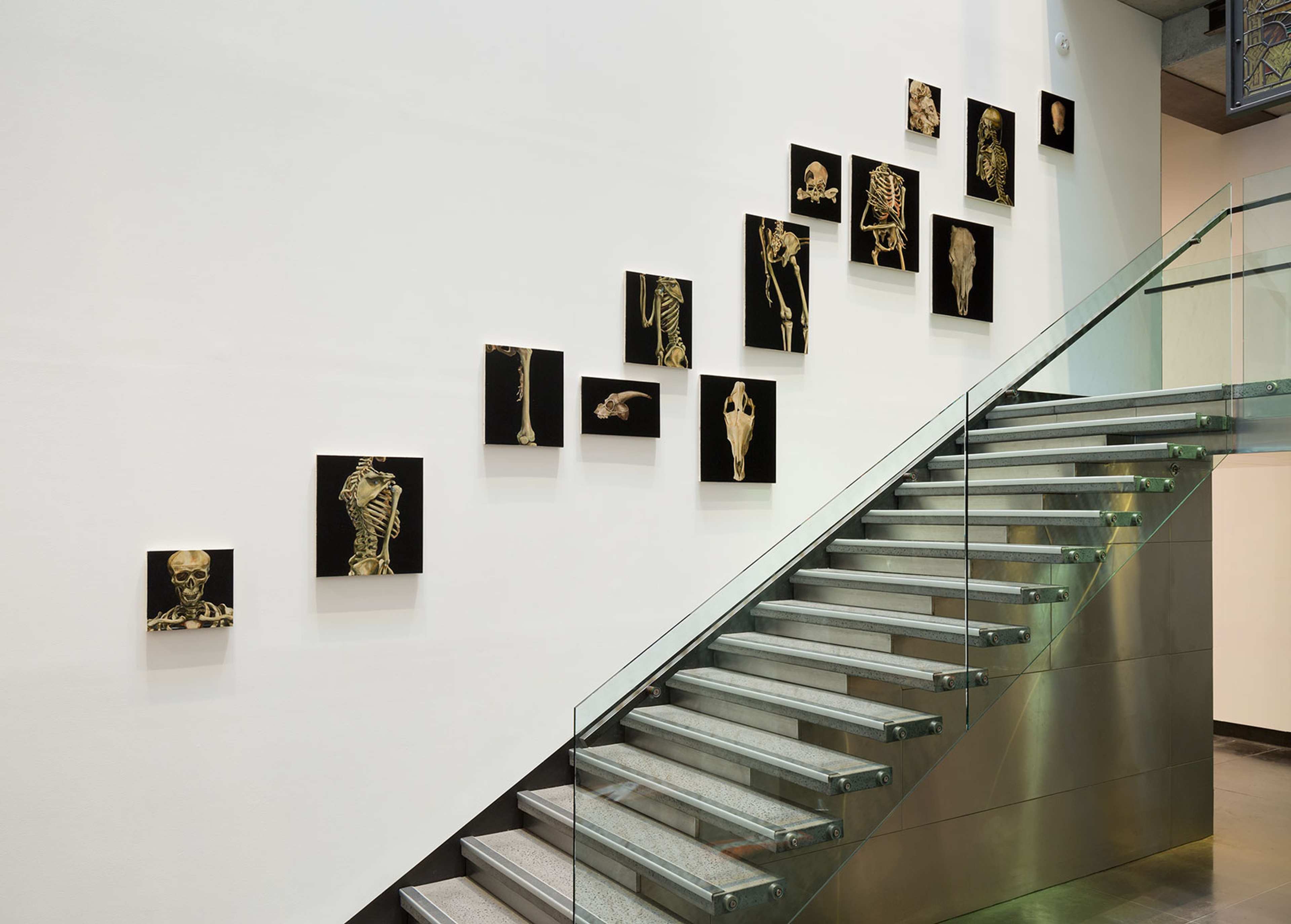 A salon hang of smaller paintings with dark backgrounds on the wall next to a staircase.