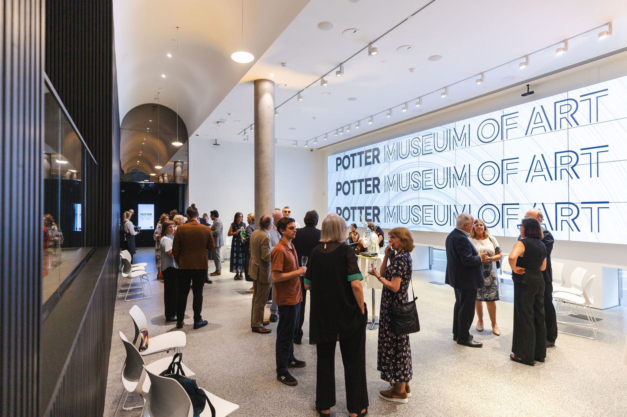 A group of people gather at an exhibition or event in front of a large wall display titled Potter Museum of Art