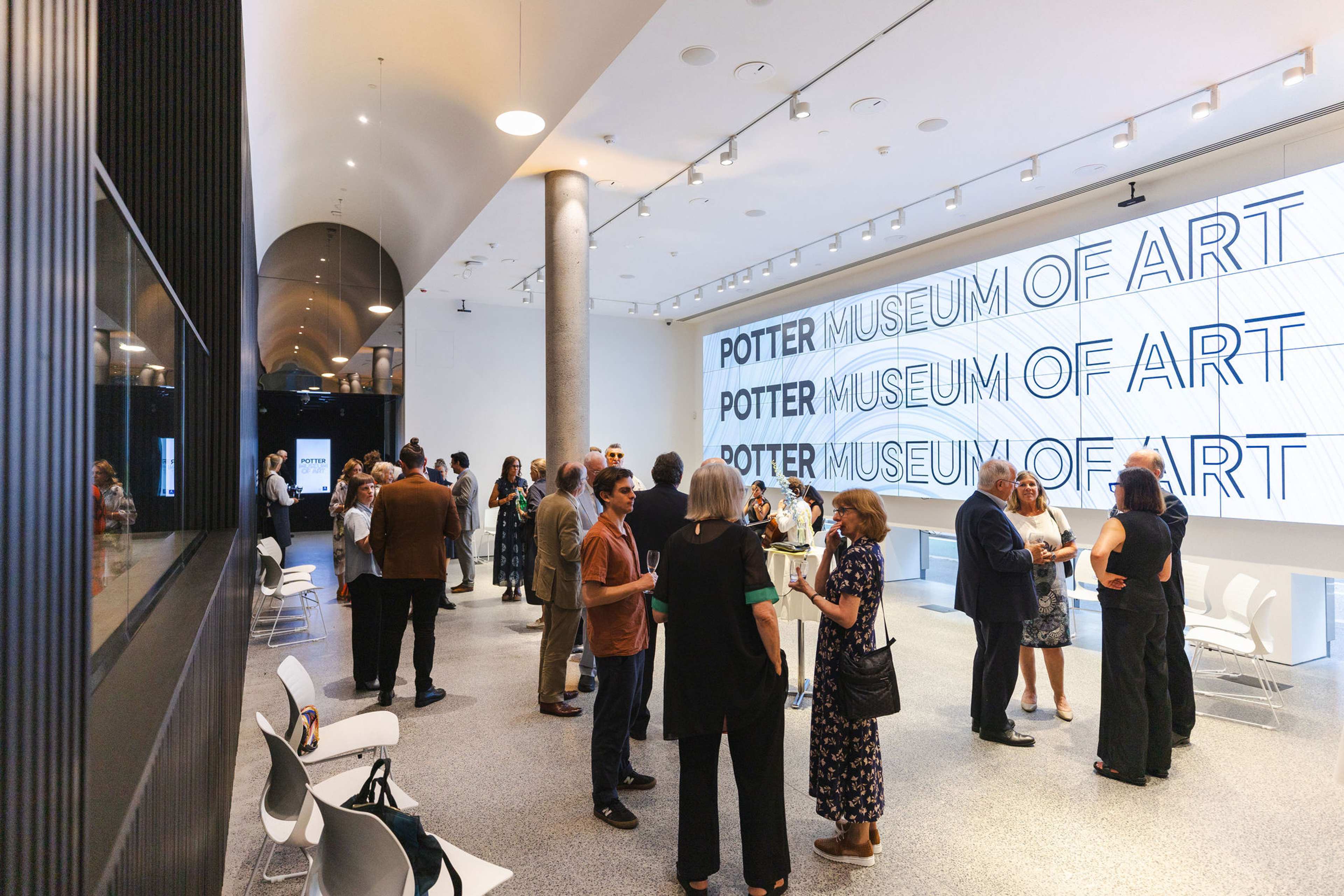 A group of people gather at an exhibition or event in front of a large wall display titled Potter Museum of Art