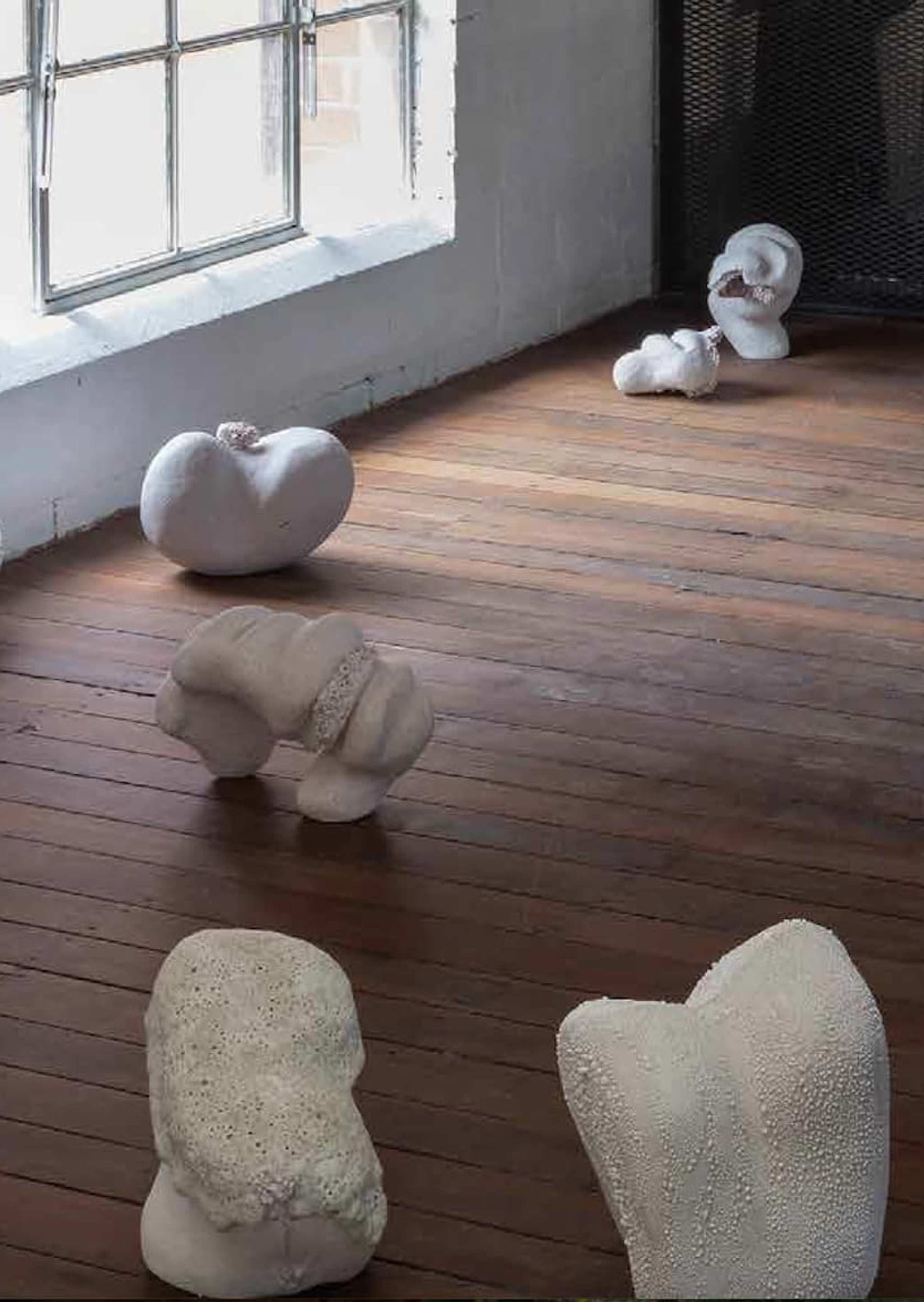 White abstract sculptures are scattered across a wooden floor near a large window, with the word “UNPREDICT” in bold yellow text on the right side of the image.