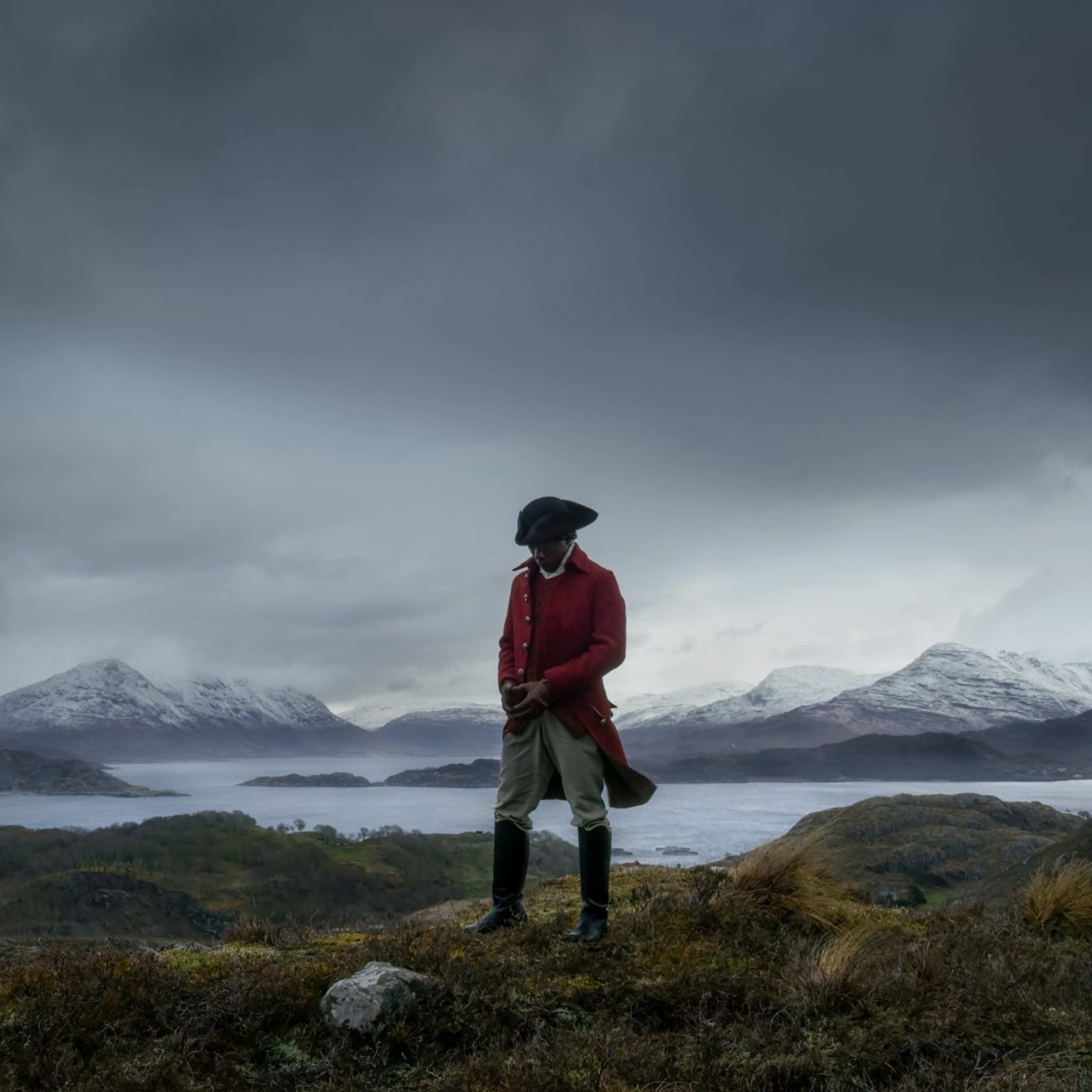 A man in a red jacket and army hat stands in a cold snowy landscape