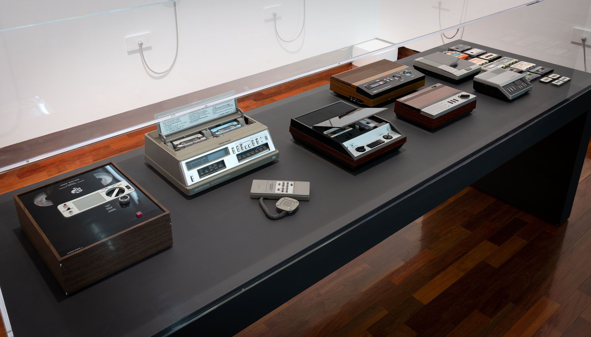 A collection of vintage answering machines and voice recorders in a vitrine