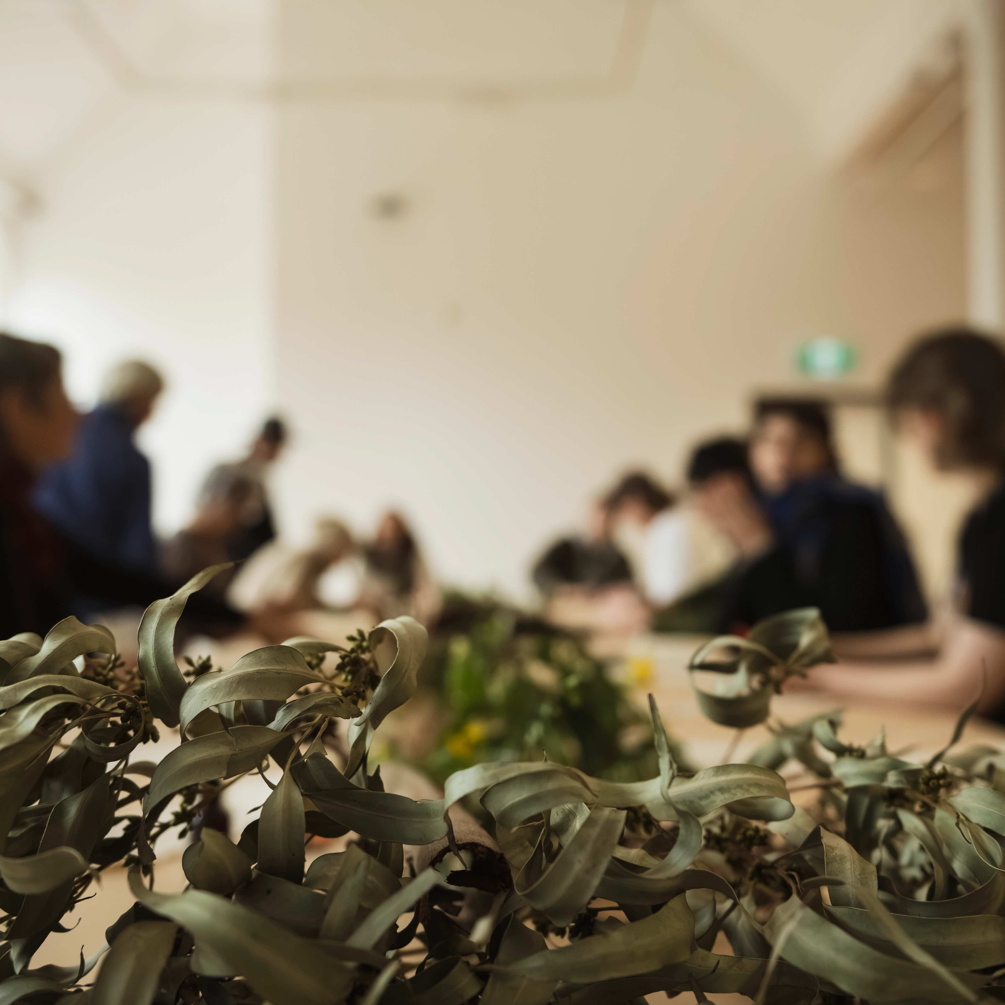 A pile of gum leaves sits on a table with figures in background