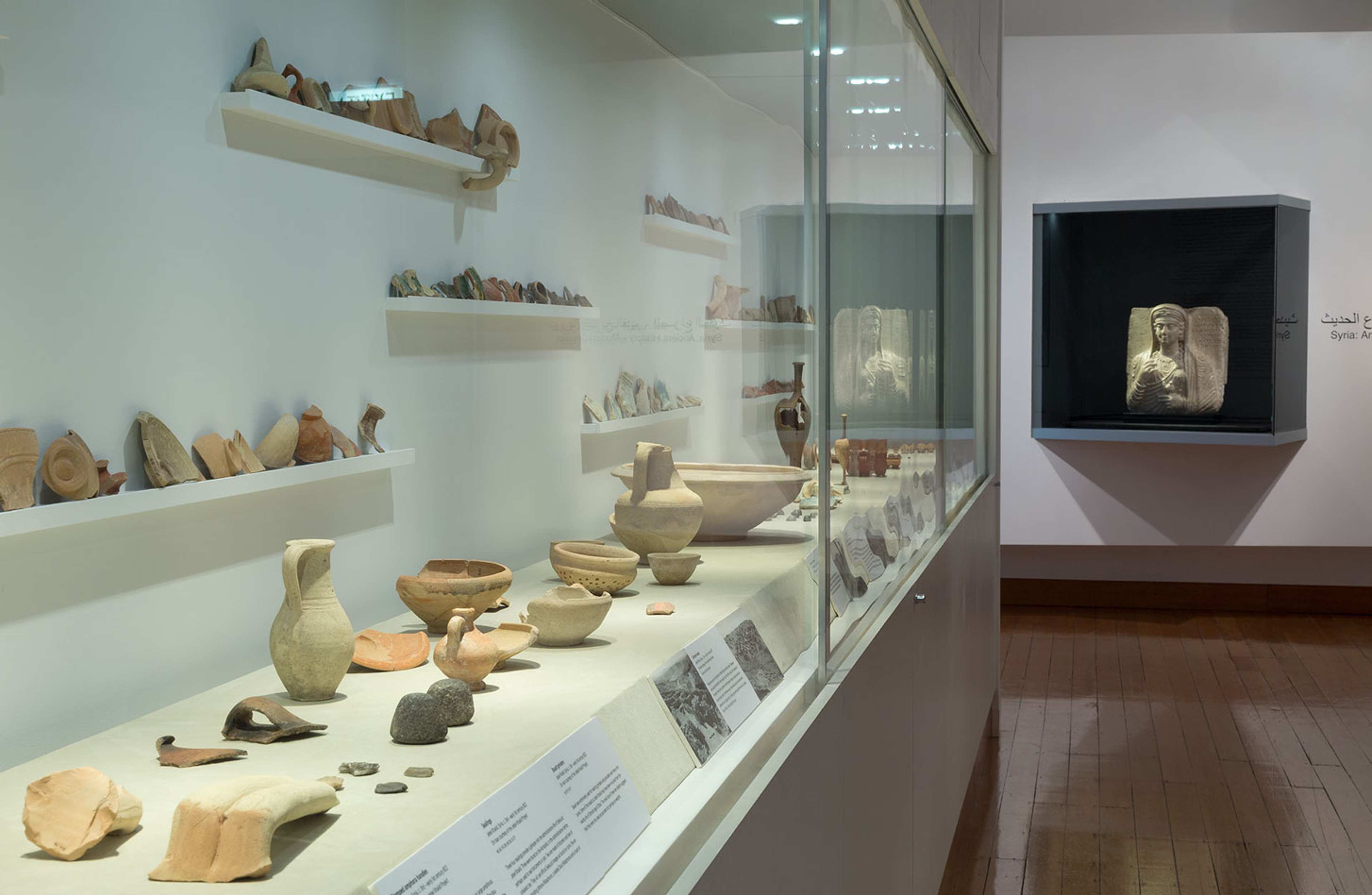 A photograph of a gallery with a large vitrine displaying a large array of ancient ceramics
