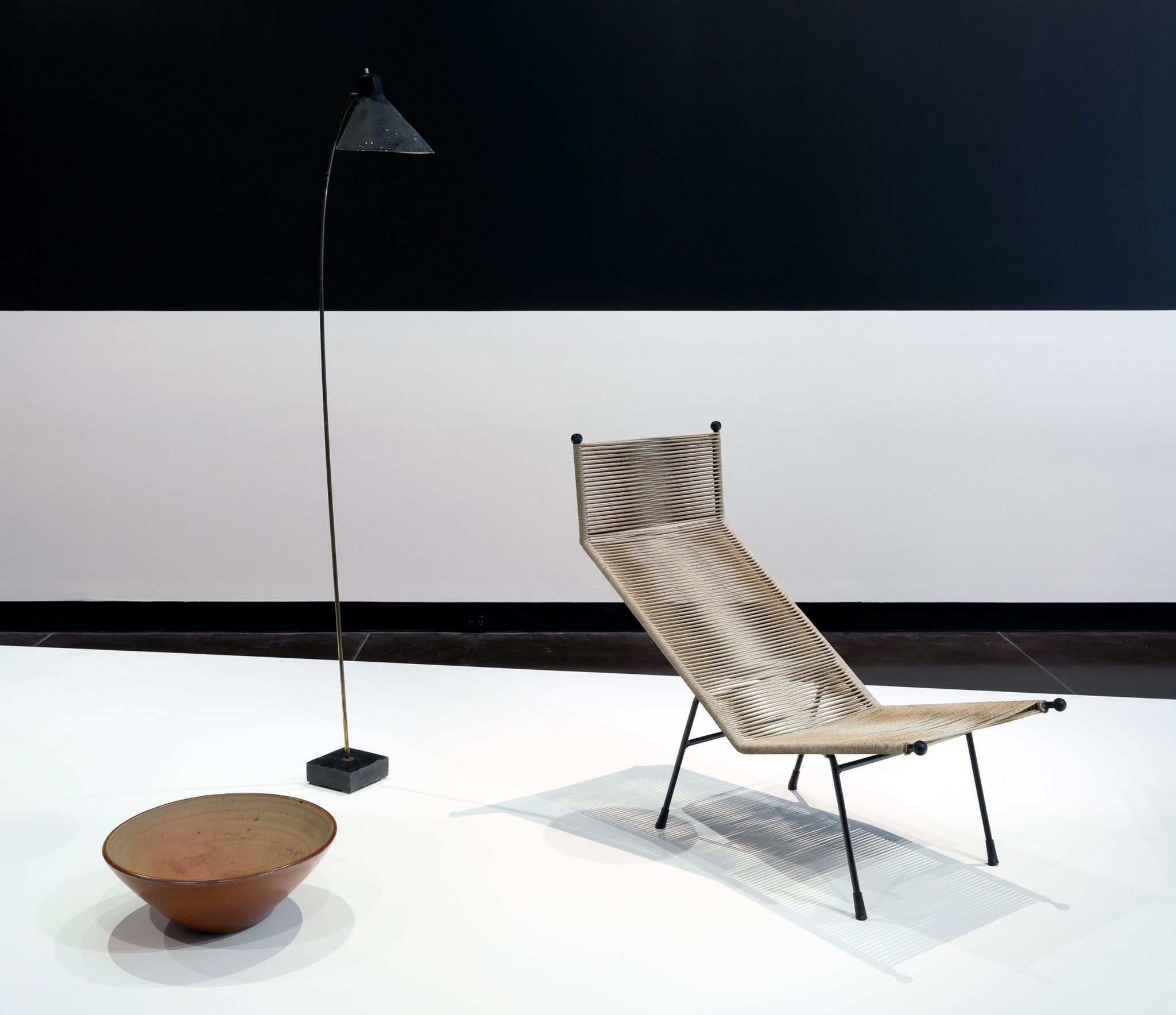 A mid century designed chair sits on a display plinthe with a lamp