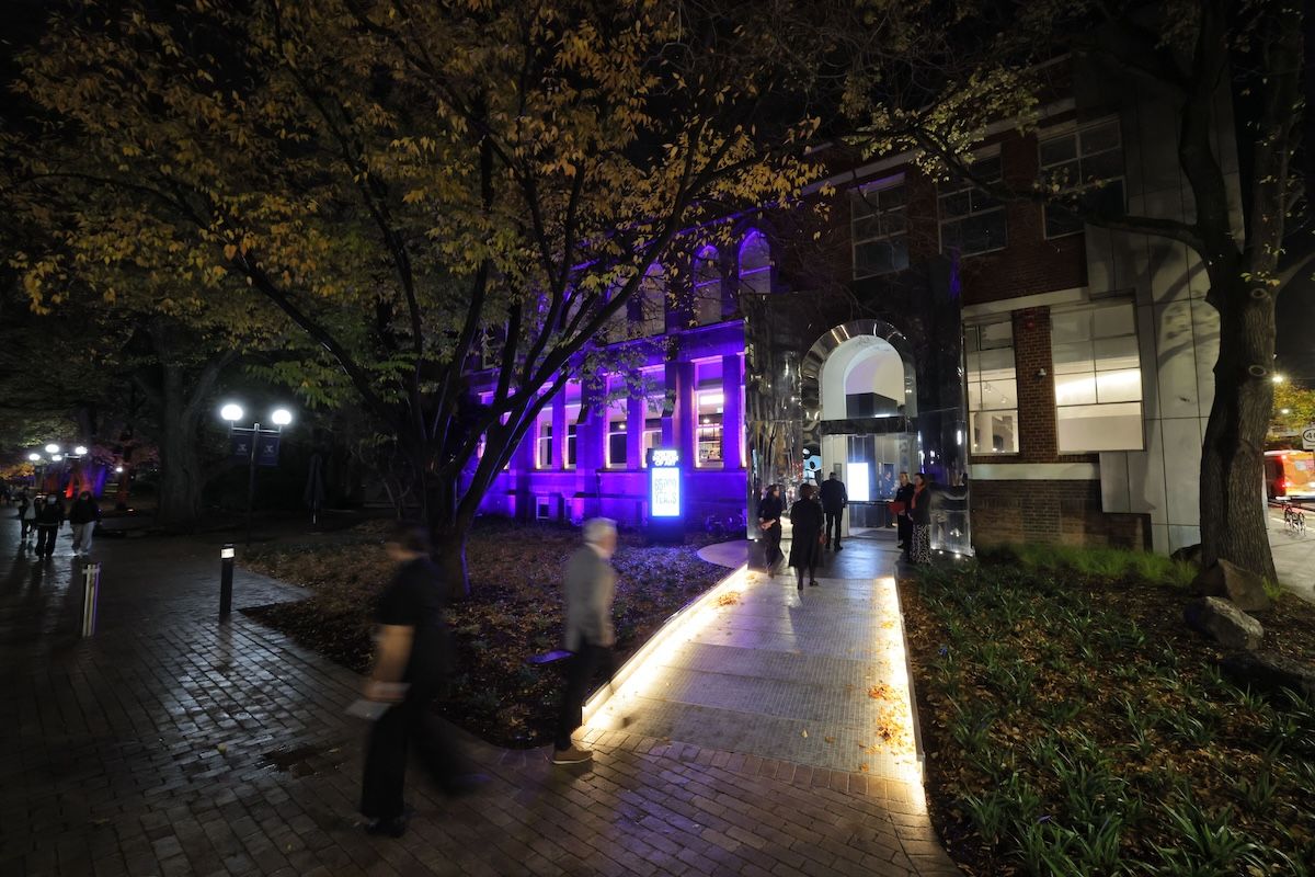 A group of people gather at an exhibition or event in front of a large wall display titled 65,000 Years: A Short History of Australian Art with text and flowers on a table beneath the sign.