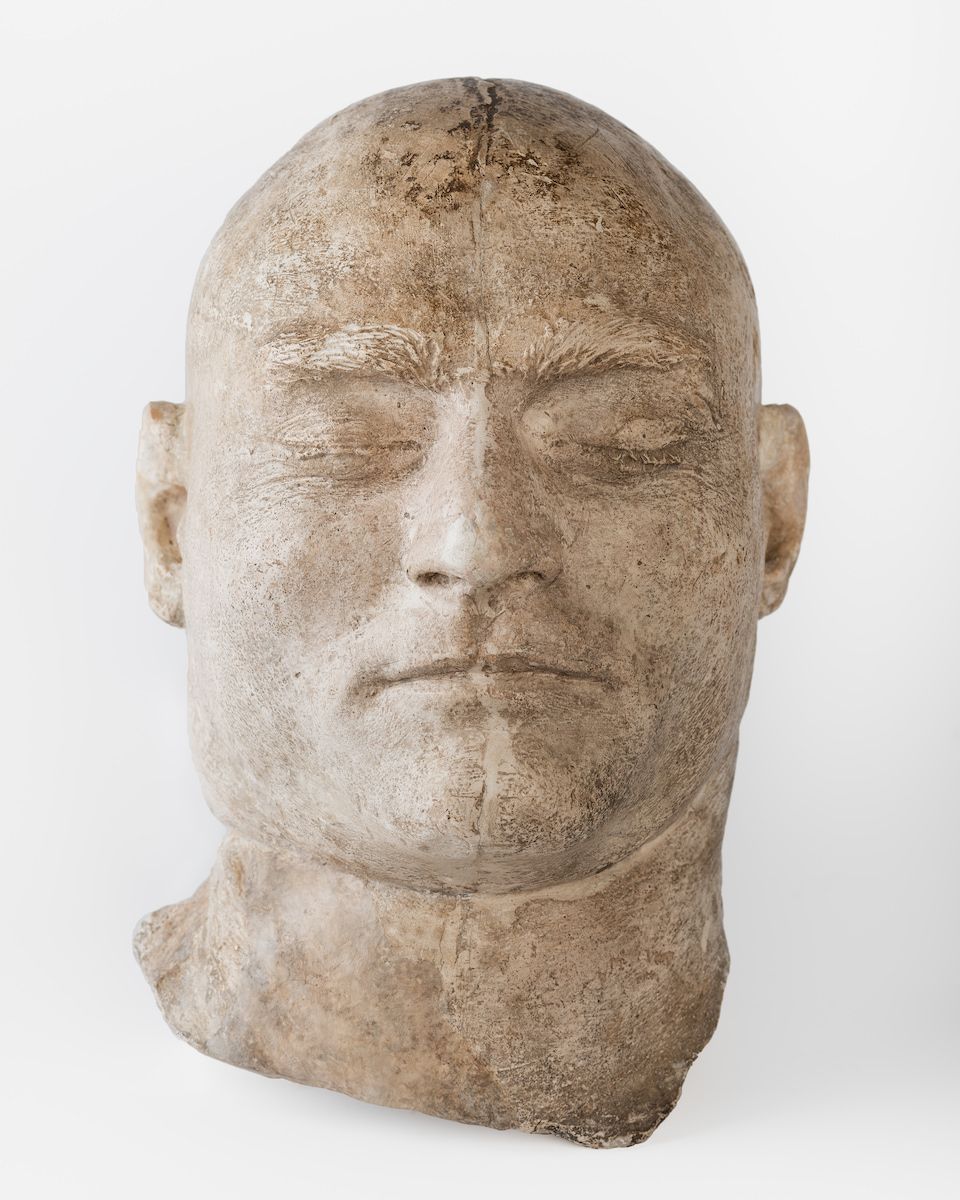 Grey plaster sculpture of a human head with wide oval face and no hair