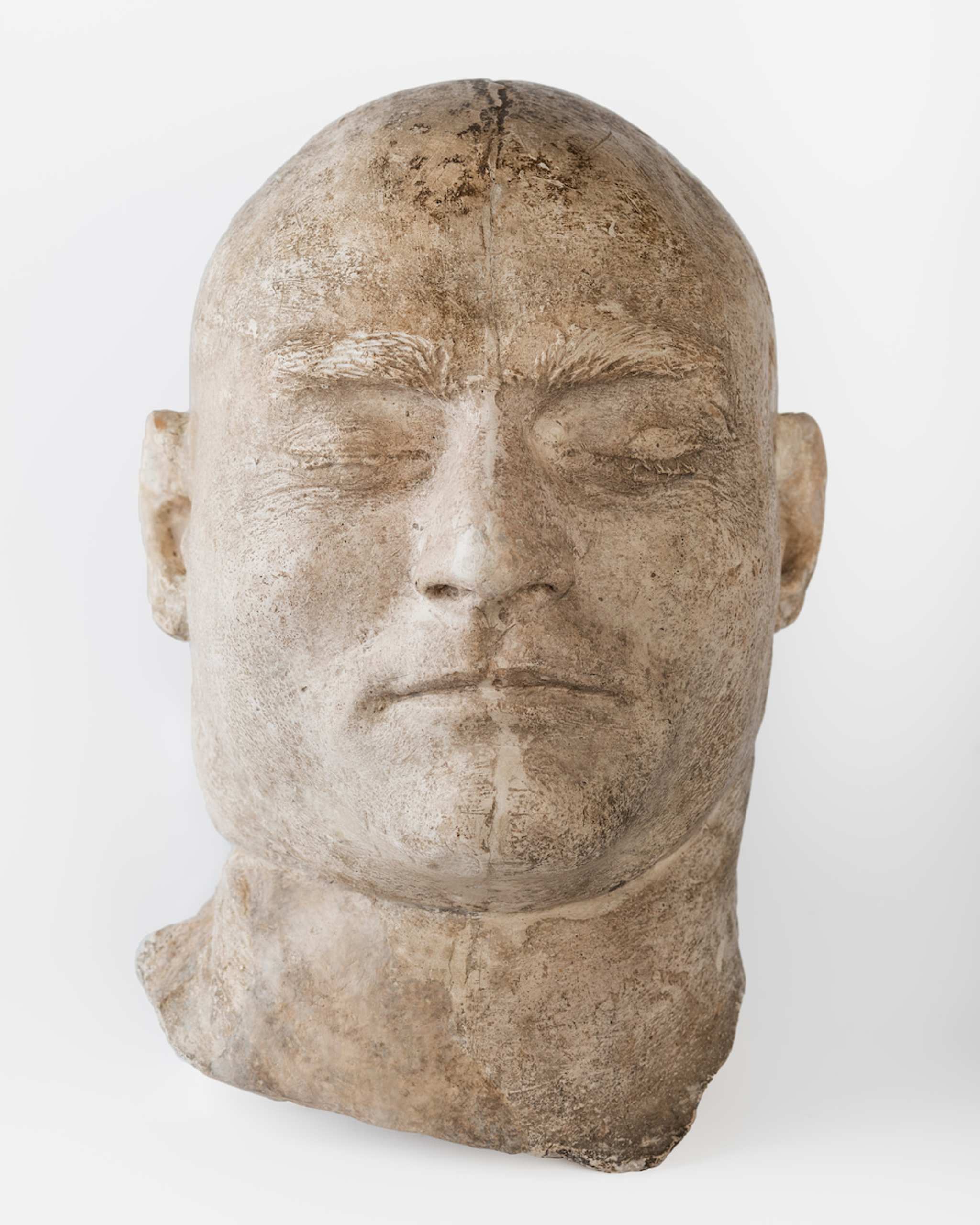 Grey plaster sculpture of a human head with wide oval face and no hair