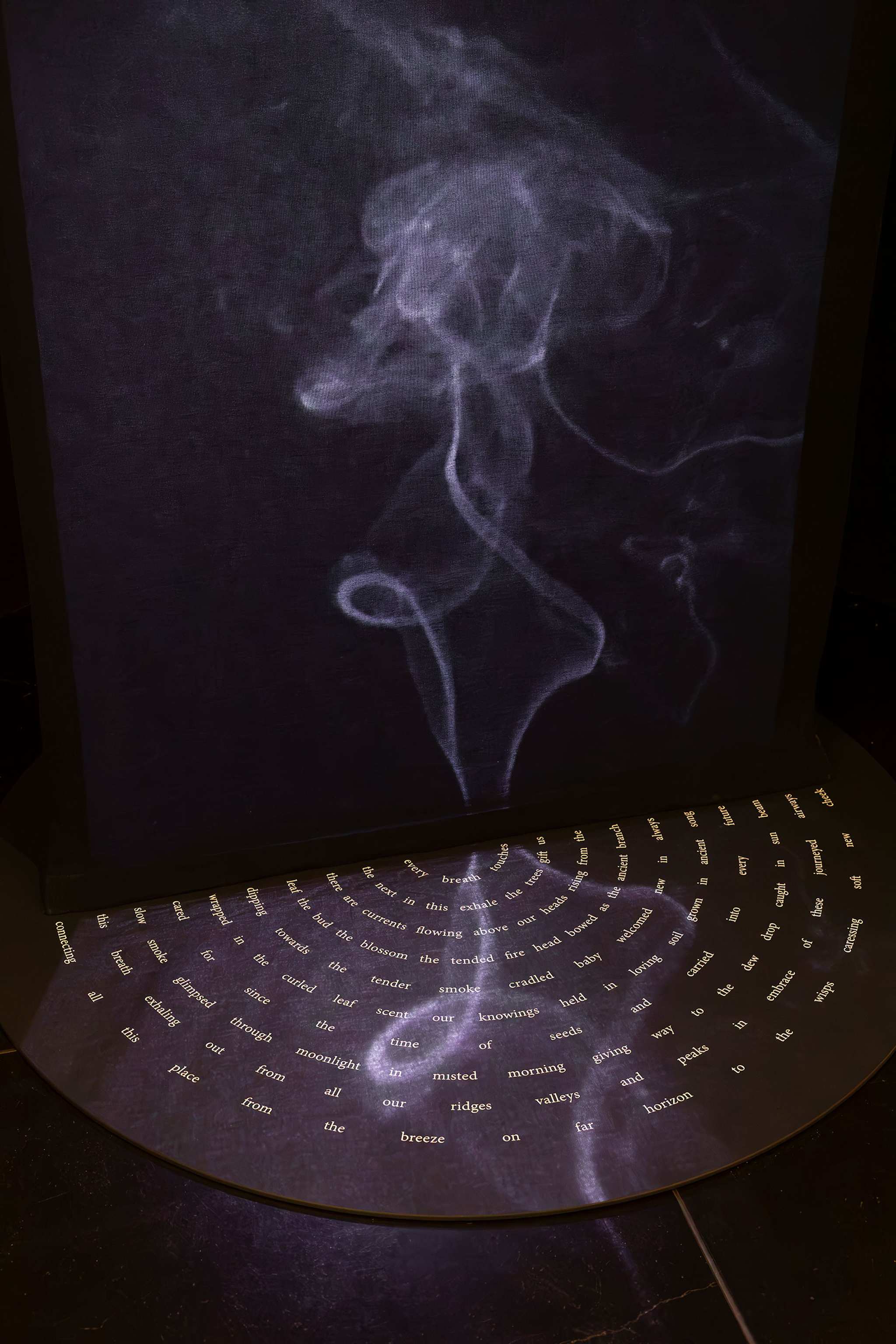A smoky, swirling white trail is projected above a curved surface covered in small, scattered words and short phrases arranged in a semi-circular pattern against a dark background.