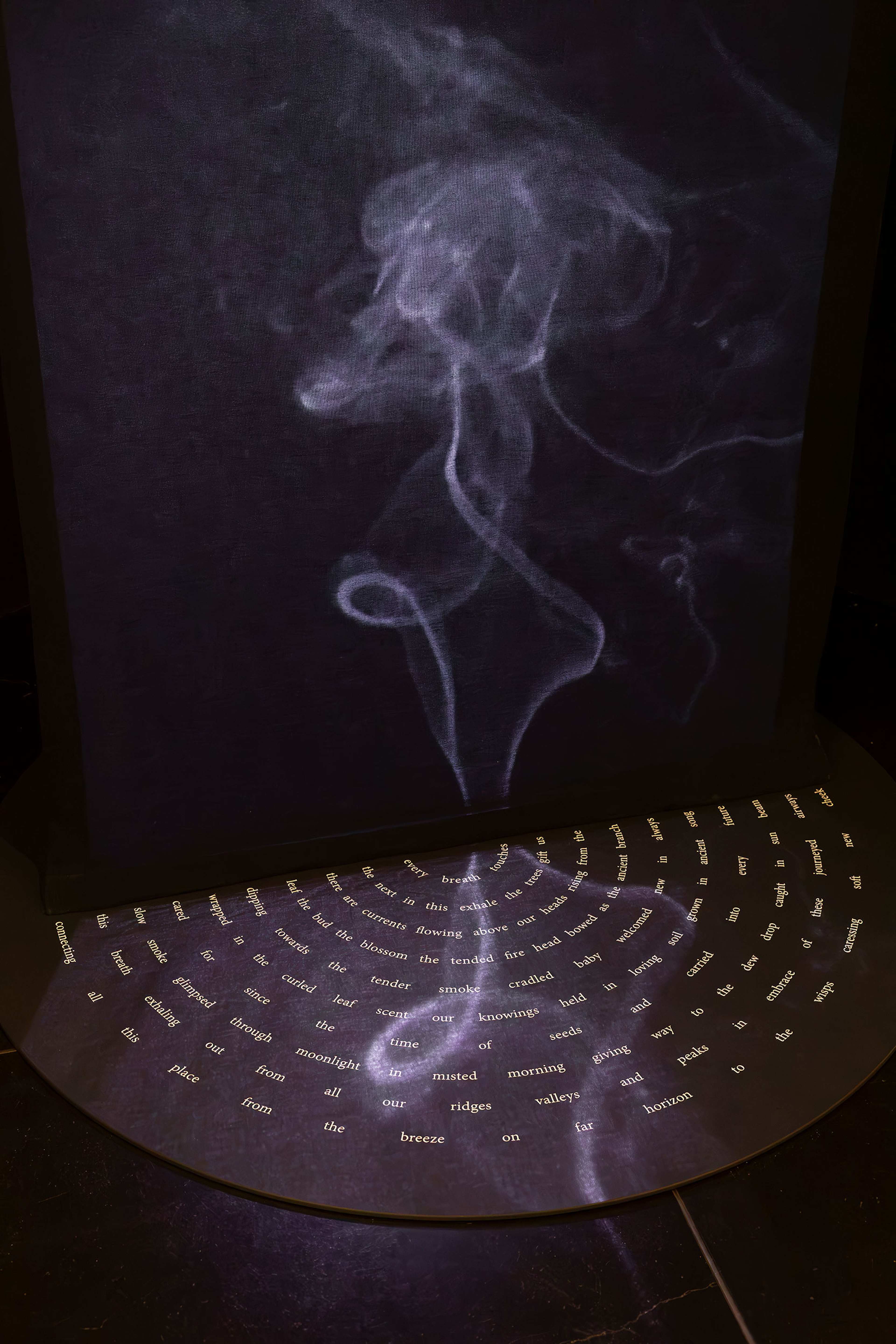 A smoky, swirling white trail is projected above a curved surface covered in small, scattered words and short phrases arranged in a semi-circular pattern against a dark background.