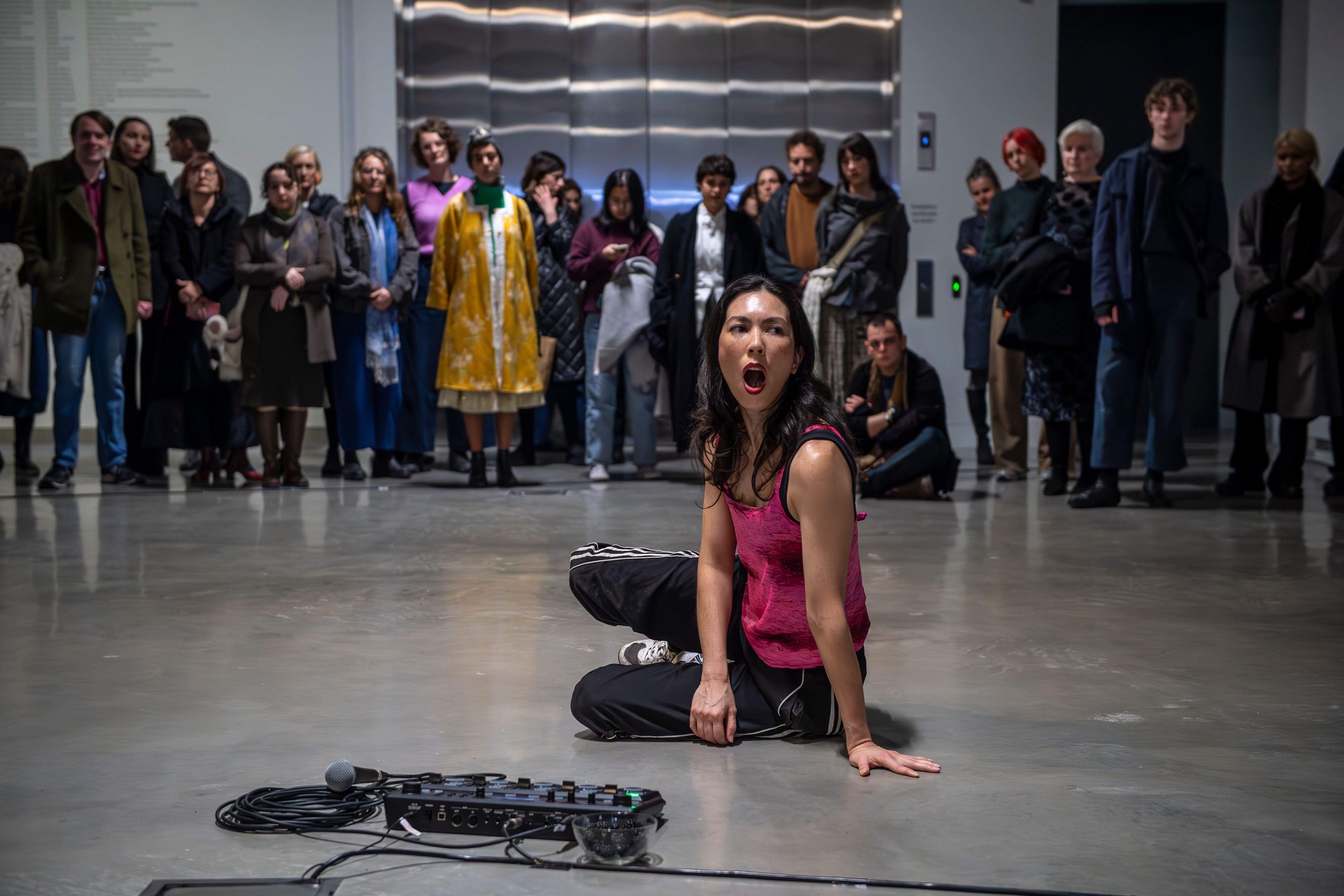 A person with mouth open sits on floor in front of a synthesiser as a crowd of people watch 