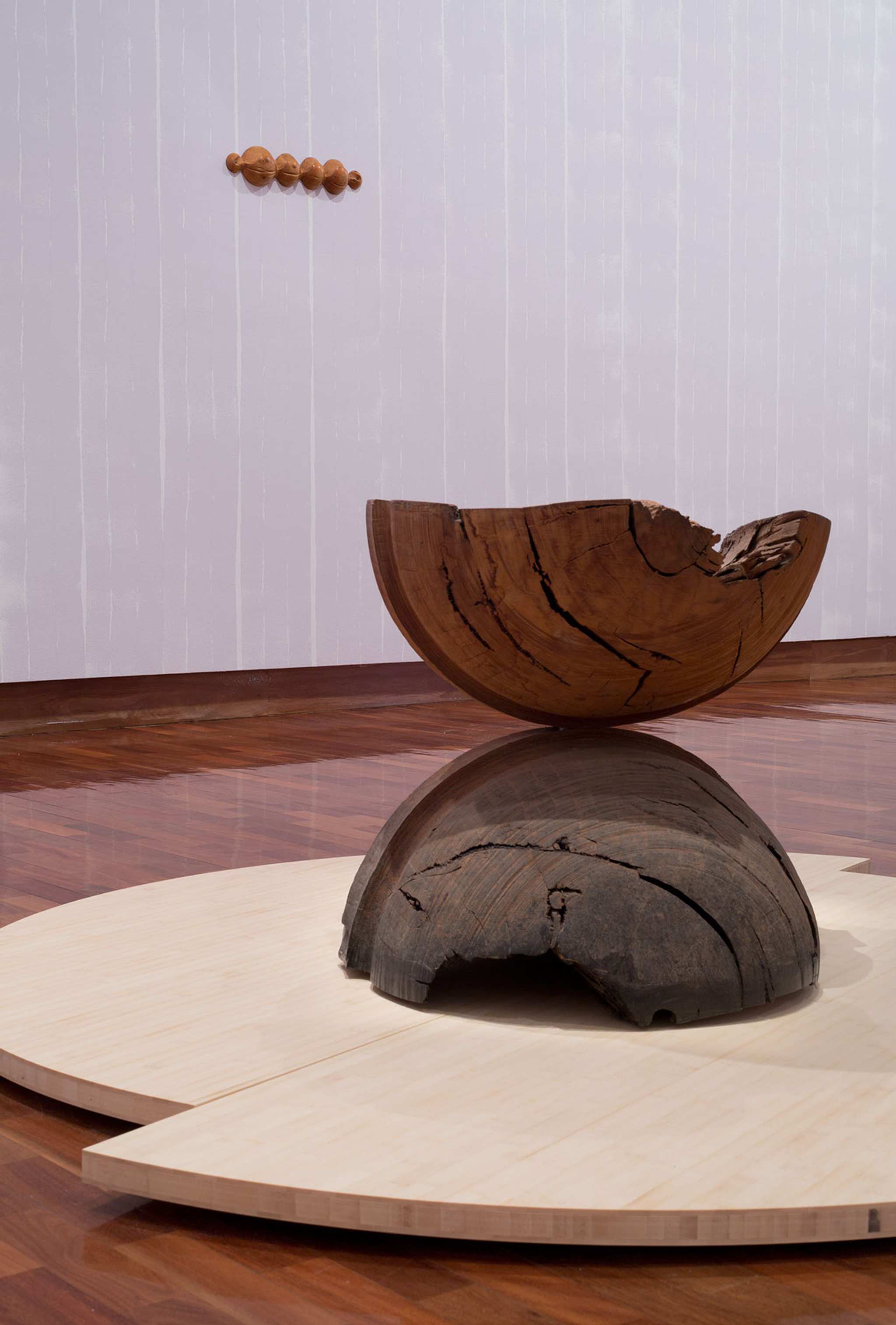 A sculpture of two brown hemispheres sits on a low plywood plinth with lilac wall behind