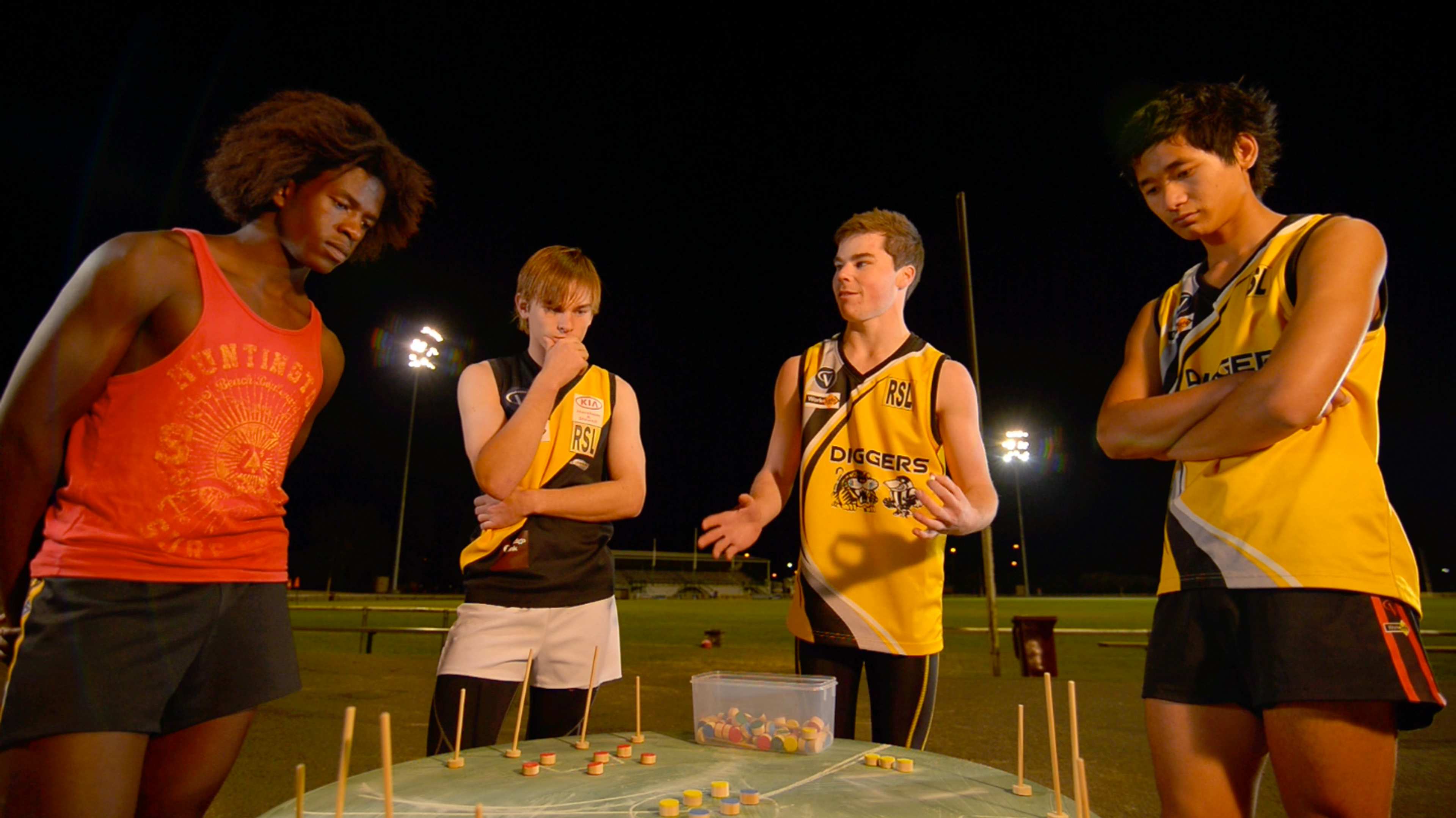 A photograph of four young people gathered around the table considering what look like a game of some kind played out on the table's surface
