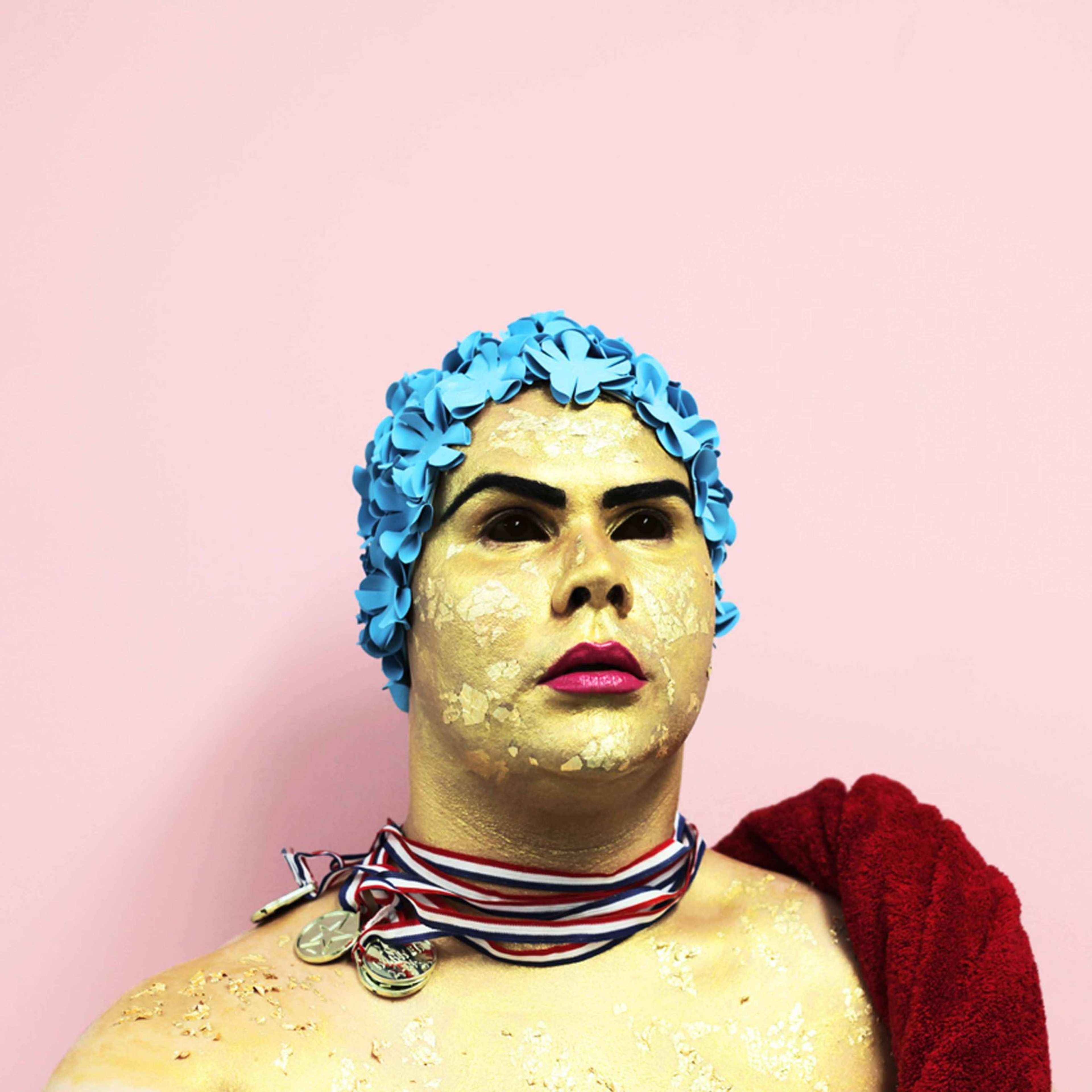 A photograph of a person in make-up wearing a tight-fitting shower cap and – on their neck – several medals swept to the side