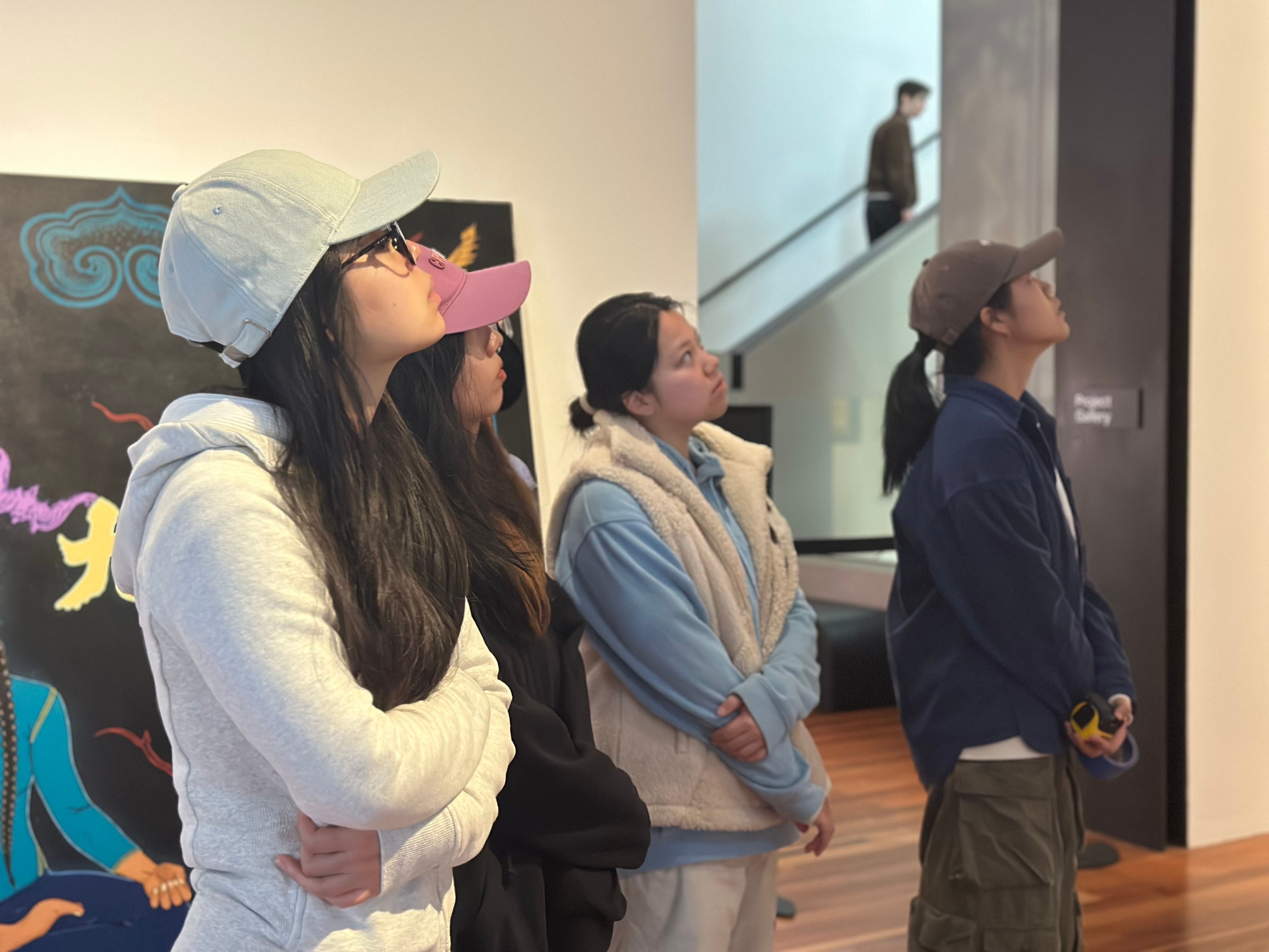 Four students looking up in a gallery space.