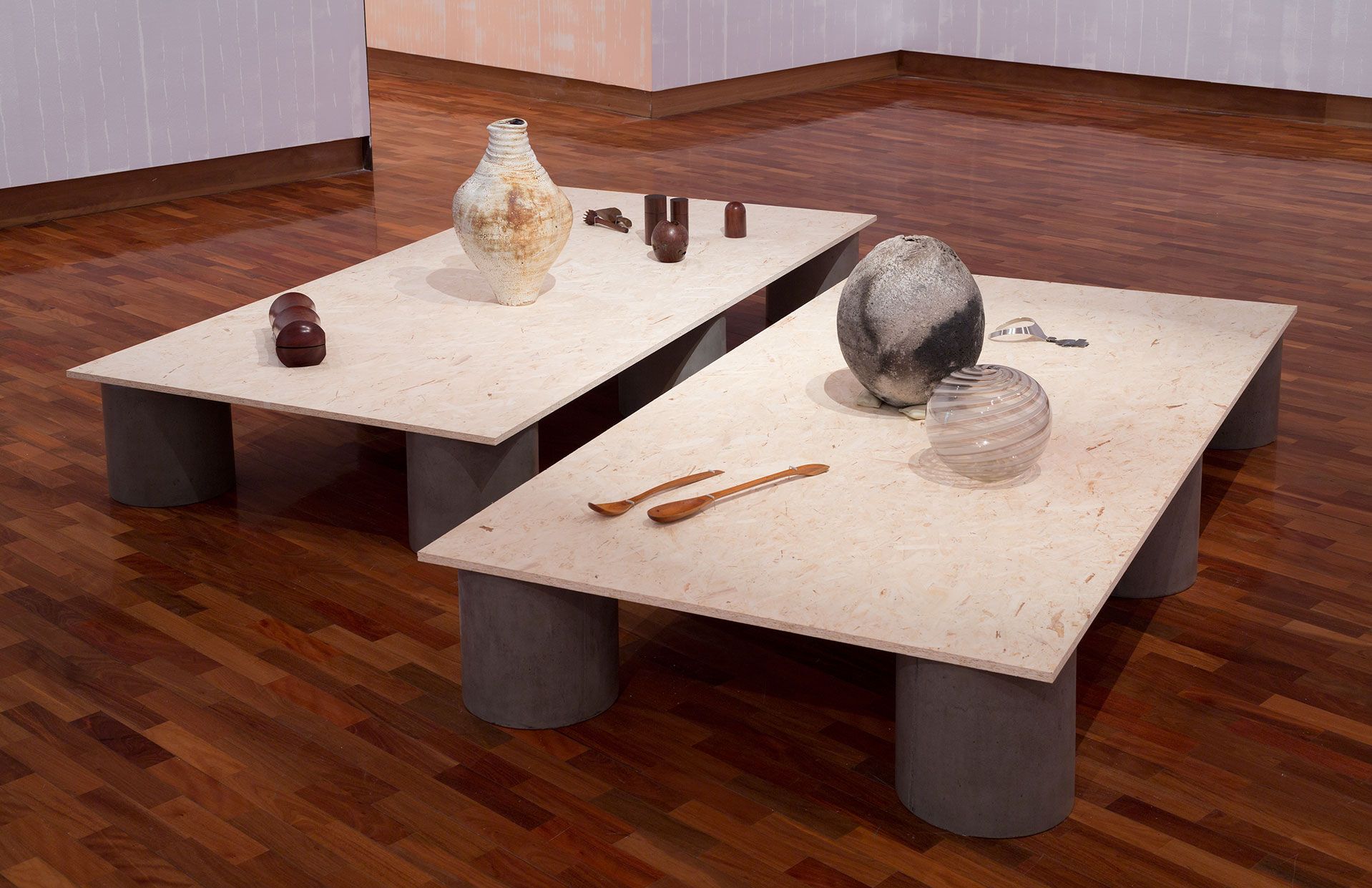 Vases and other decorative objects made from various materials are displayed on low plywood tables. 