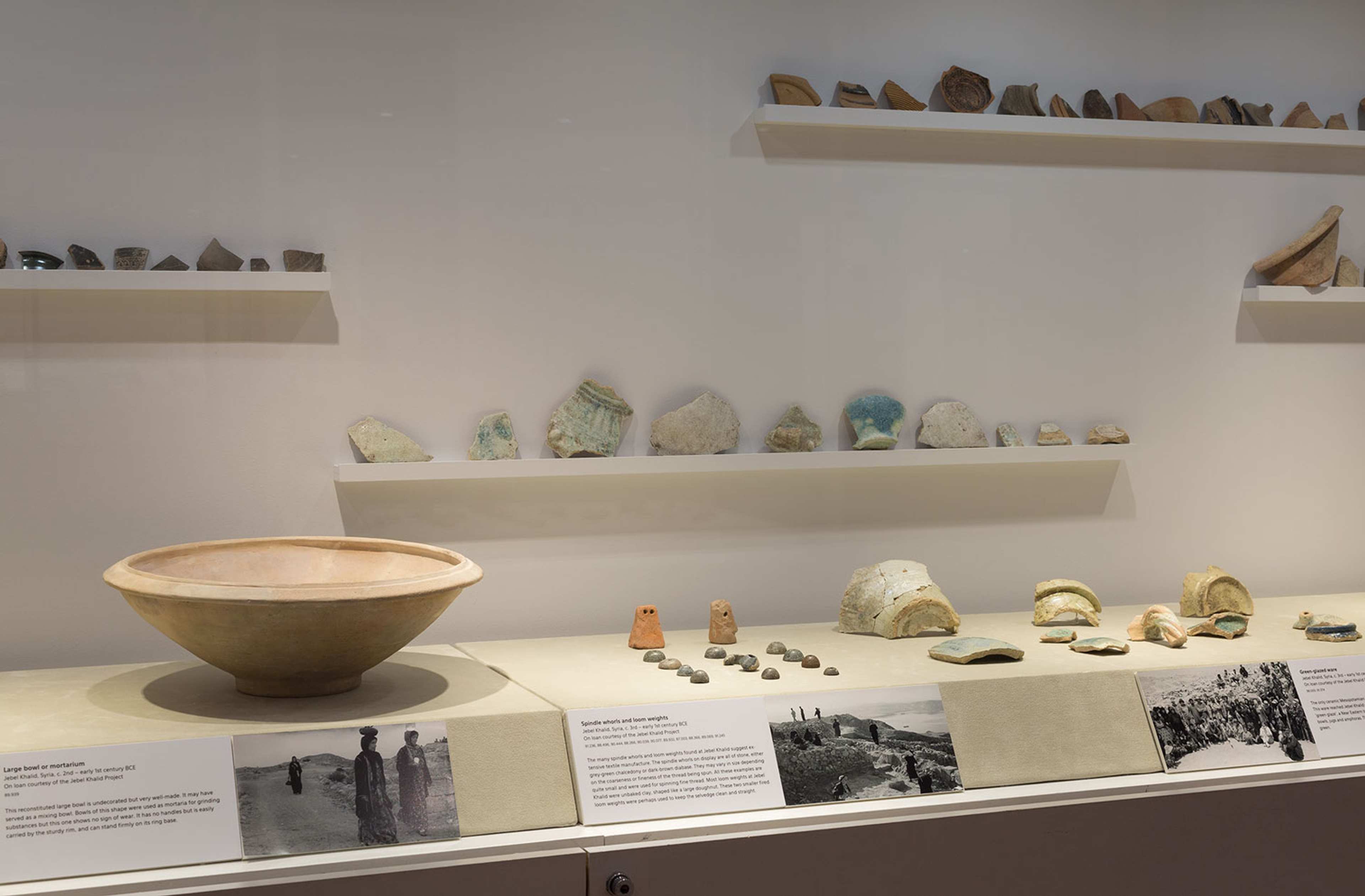 An image of a vitrine displaying an ancient ceramic vessel and various ceramic fragments arranged in rows