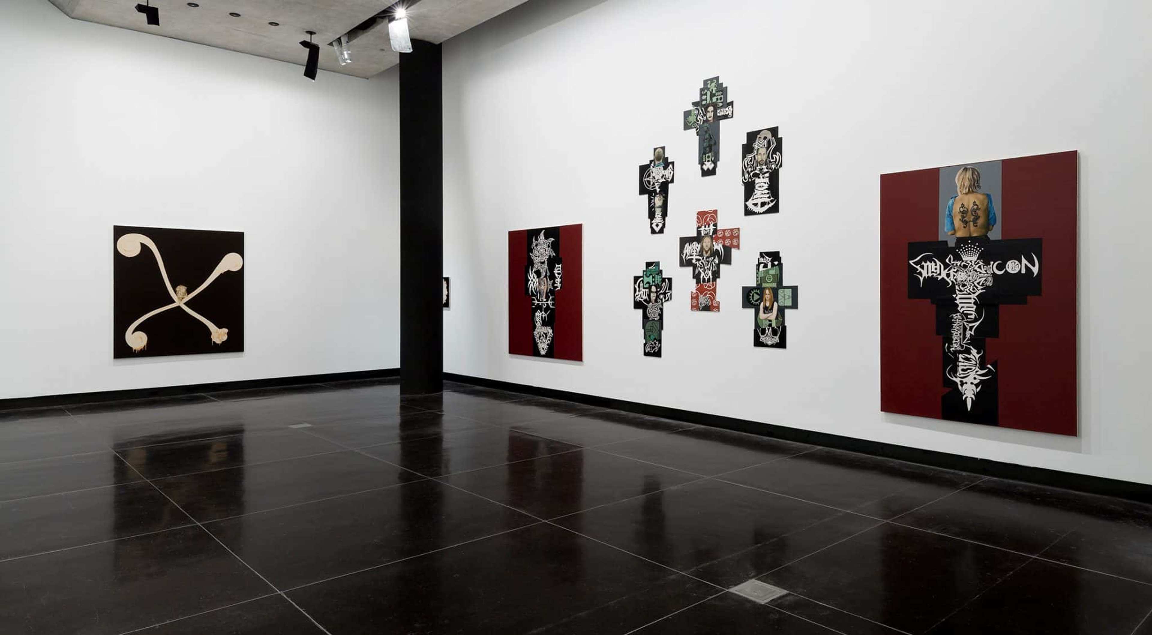 Three large abstract canvases in the shape of crosses or featuring motif of the cross in black, brown and red hang in the gallery space with white walls