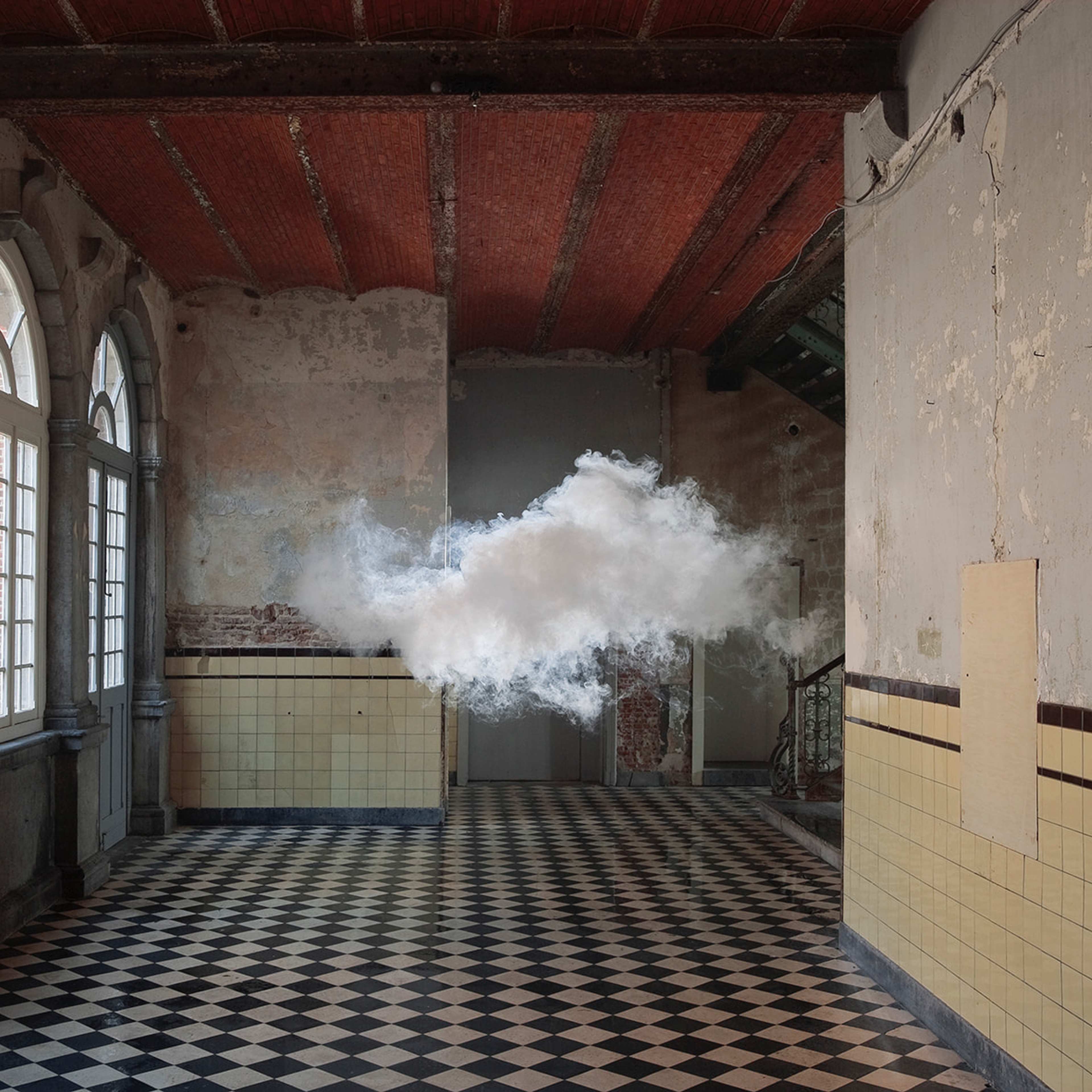 A dense cloud of smoke hanging in the centre of a room with arched windows and ornate tiled floor