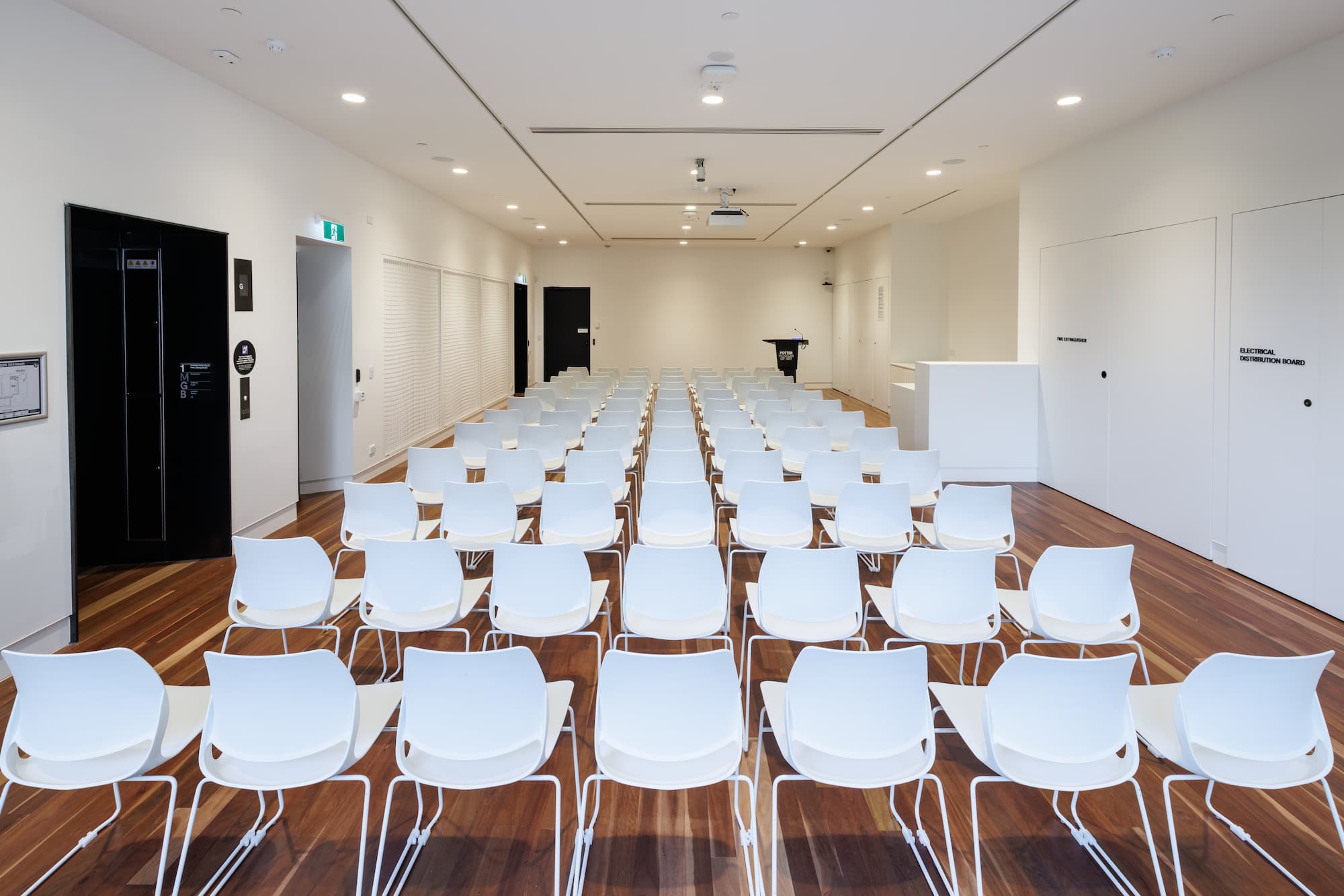 A long white room with lines of chairs facing a lectern at the front