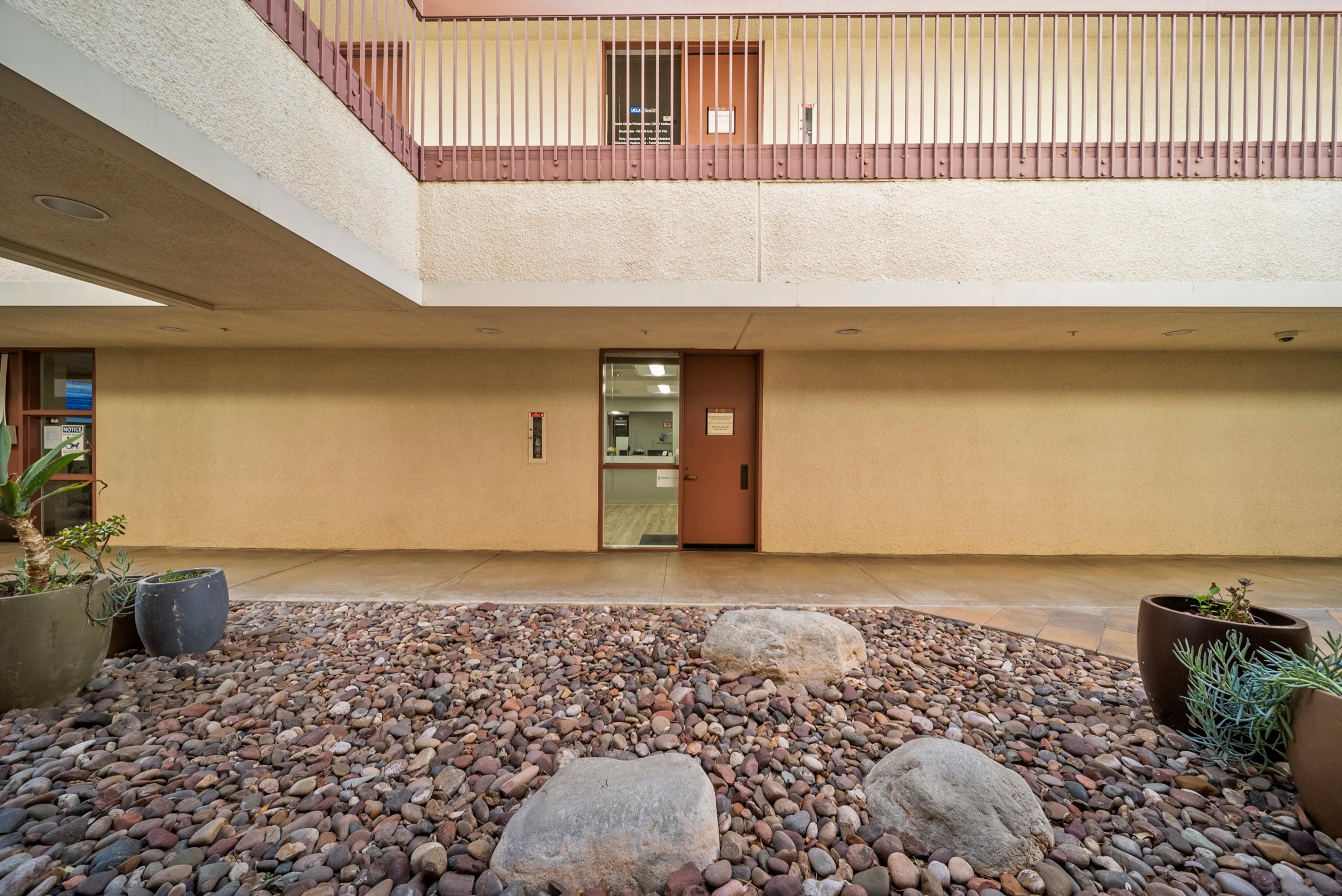 The building’s courtyard outside the practice entrance (suite E-12), with river-rock landscaping, boulders, and succulent planters.