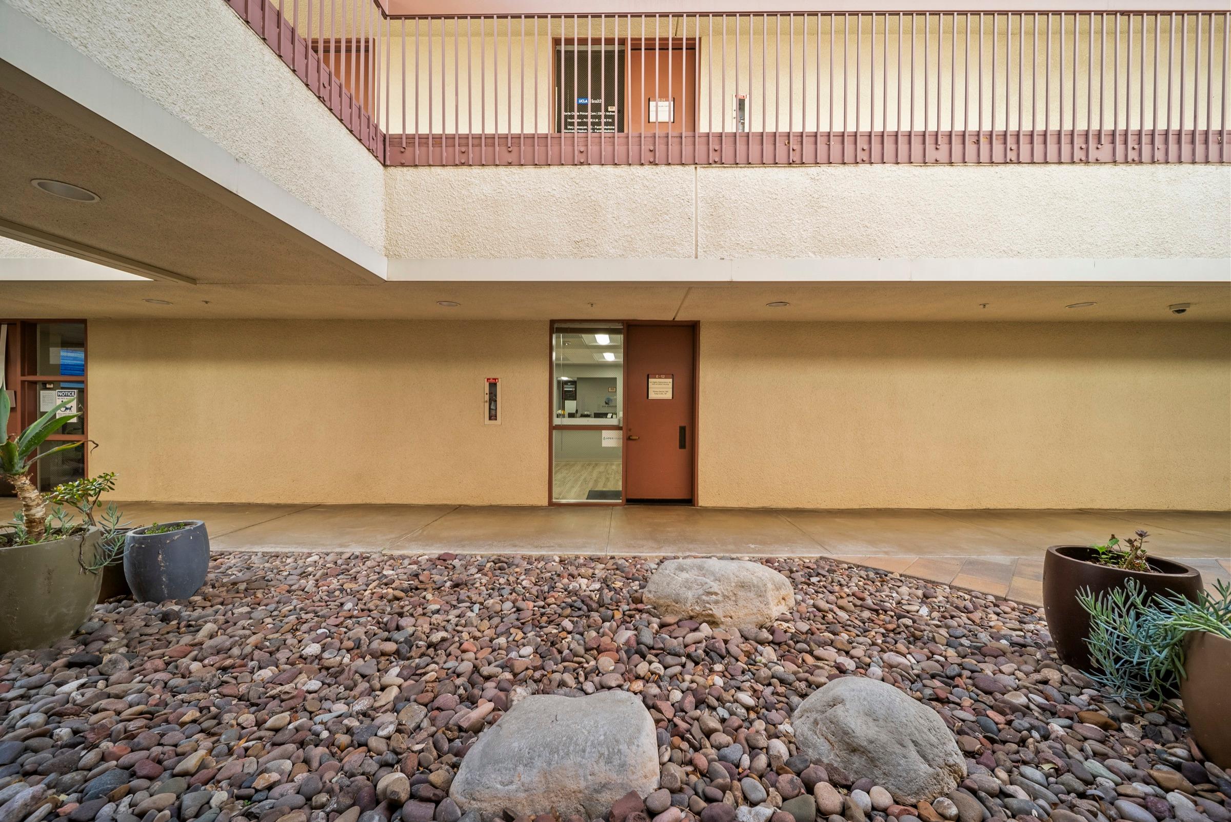 The building’s courtyard outside the practice entrance (suite E-12), with river-rock landscaping, boulders, and succulent planters.