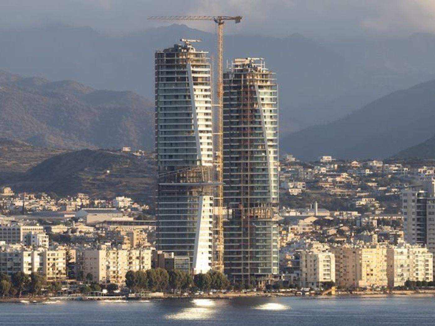 Limassol waterfront skyline with high-rise buildings and mountains behind the city.