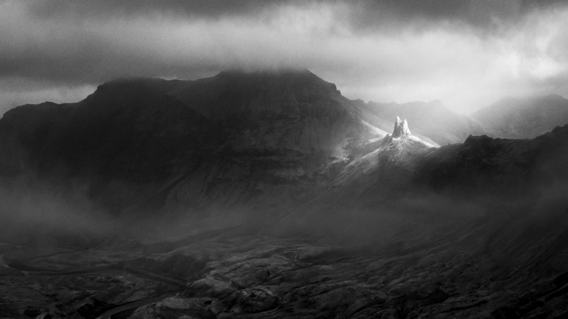 Black-and-white mountain landscape with a sunlit rock spire piercing through drifting clouds and mist over a shadowed valley.