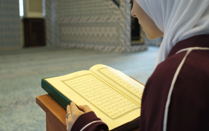 Seorang wanita muslimah sedang tersenyum teduh dengan latar belakang pemandangan yang menenangkan dan islami.