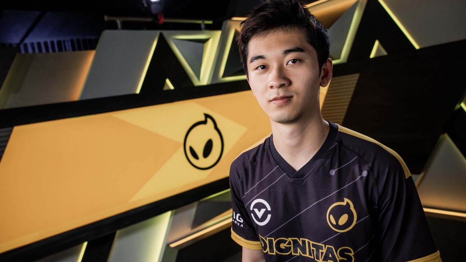 Close up of League of Legends player Biofrost in his black Dignitas jersey who faces the camera with a slight smile and the Gignitas logo behind him in yellow