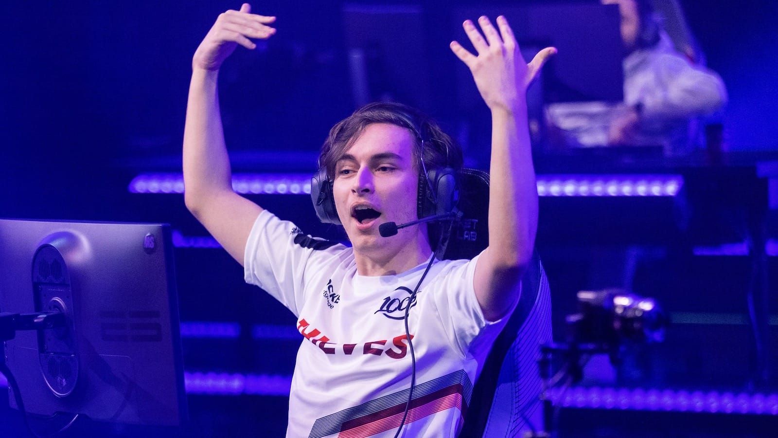 100 Thieves Valorant player Asuna sits on a chair onstage and raises his arms up in joy