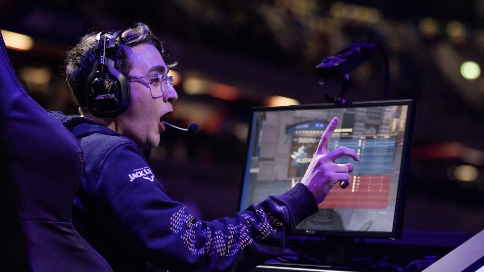 Side view of Call of Duty League player Clayster behind his monitor with his mouth open excitedly and holding one finger up