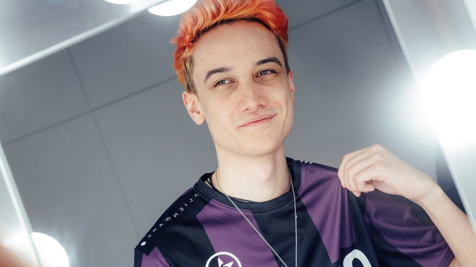 Close-up of League of Legends player Biopanther with a slight smile as he looks at himself and tugs at his jersey around his shoulder in a mirror