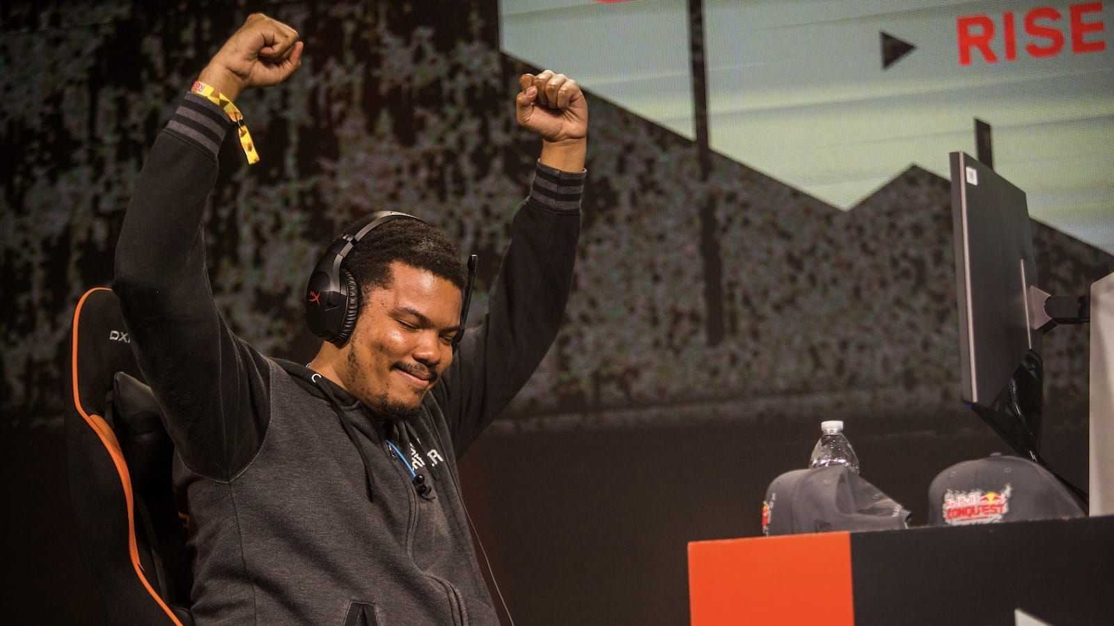 Fighting game player Hotashi on stage raises his arms up and looks down smiling after big play
