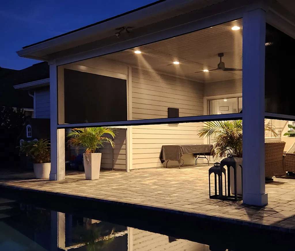 SunPro motorized screen lowered on a covered lanai beside a pool in the evening light.