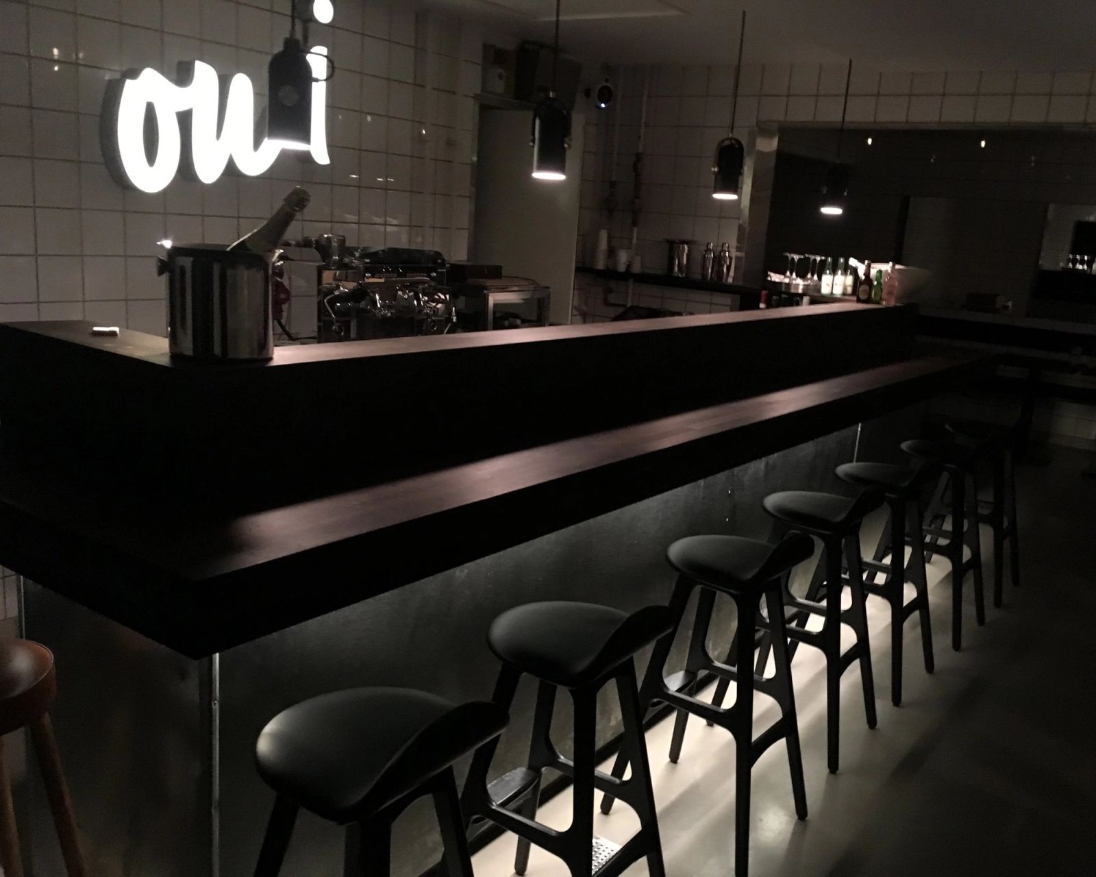 Interior design af moderne bar med sort theke, barstole og neon-skiltning i minimalistisk französk bistro