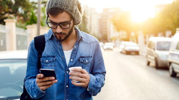 Mand i denim jakke på gaden kigger på smartphone — branding, identitetsdesign og digital markedsføring for Zenegy