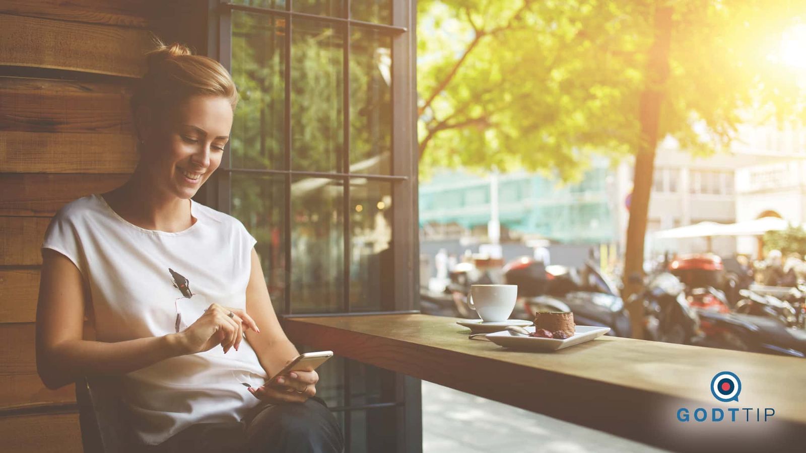Interface design showcasing visual identity: Woman using smartphone at café table with coffee and pastry in golden sunlight