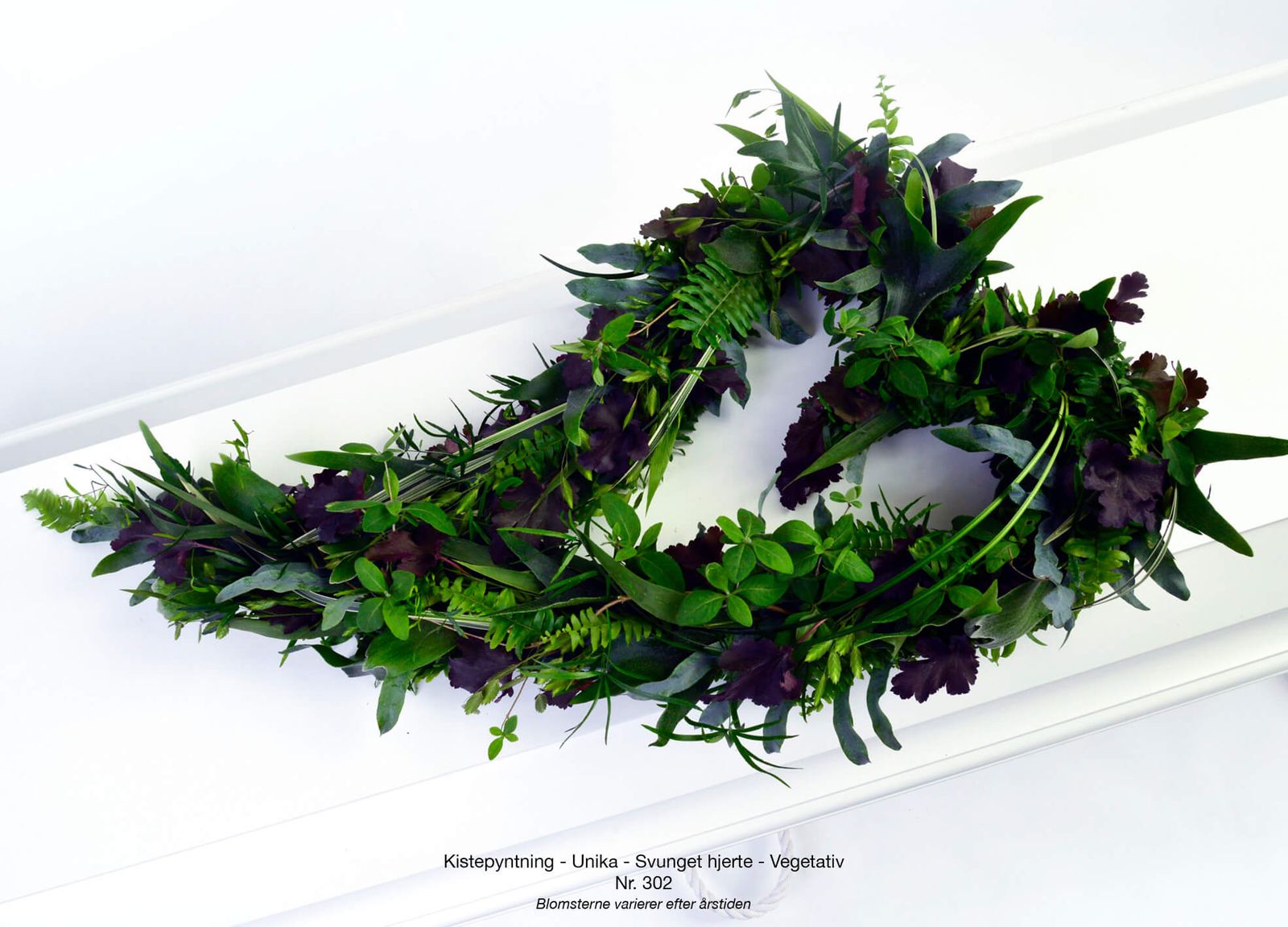 Wreath arrangement featuring purple and green foliage styled for memorial floral catalogue presentation