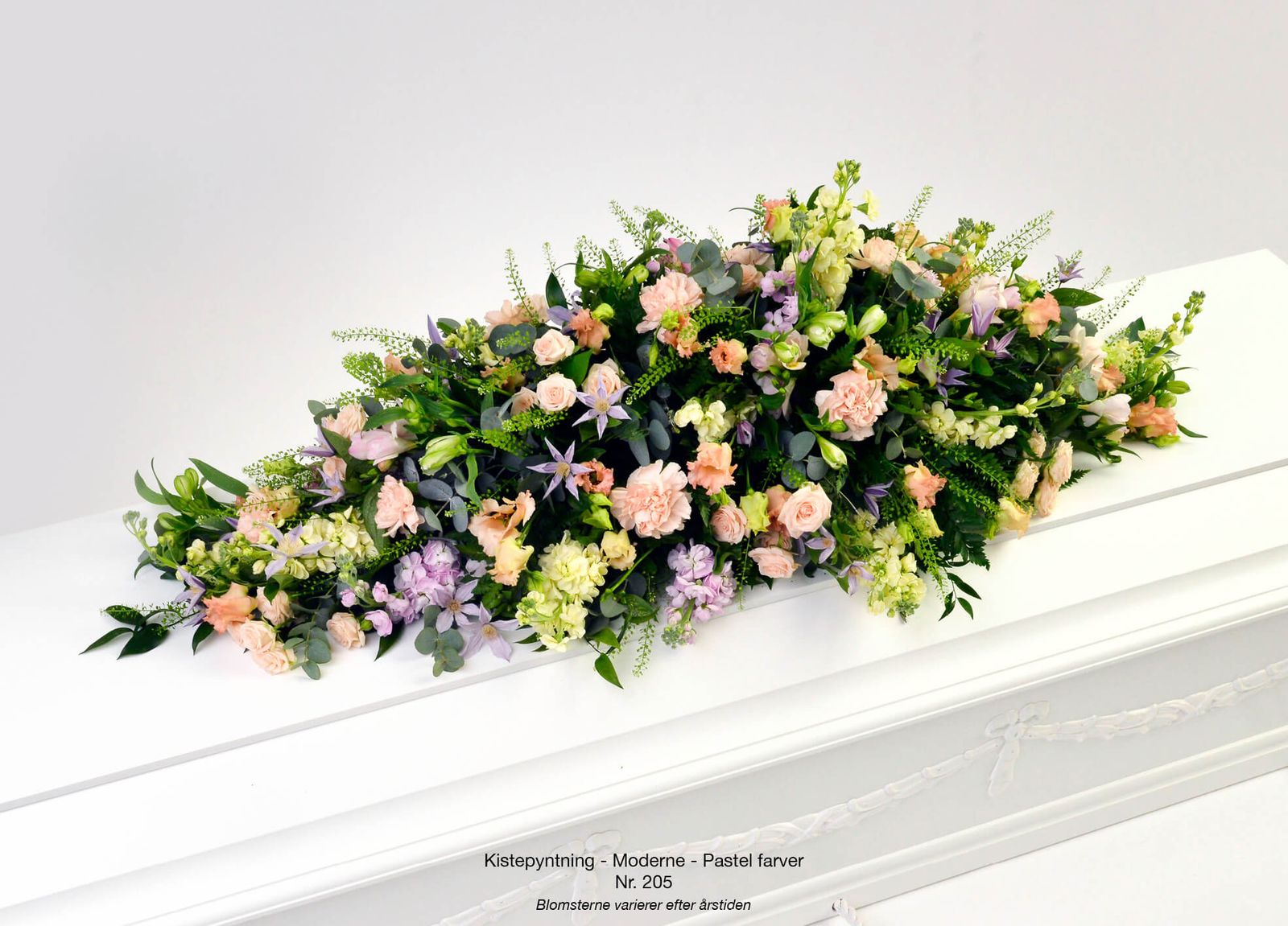 Art direction of casket spray arrangement featuring peachy roses, purple accents and lush greenery for funeral catalog
