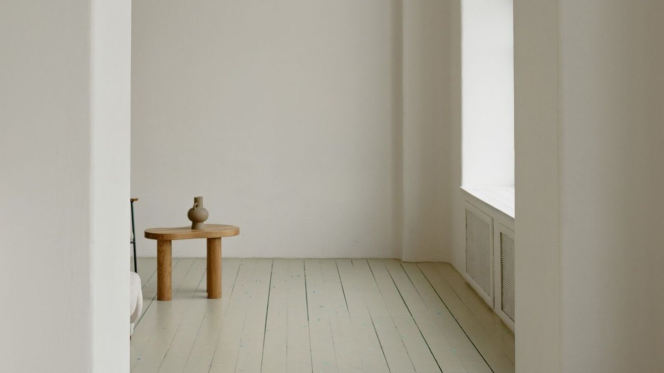 A plain white archway opening onto a sunlit room with a small wooden stool.