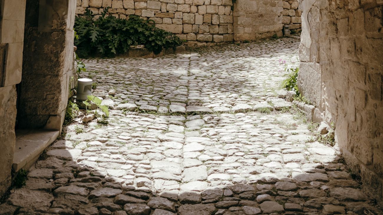 Sunlit stone passage opening onto a cobbled courtyard with pale walls and greenery