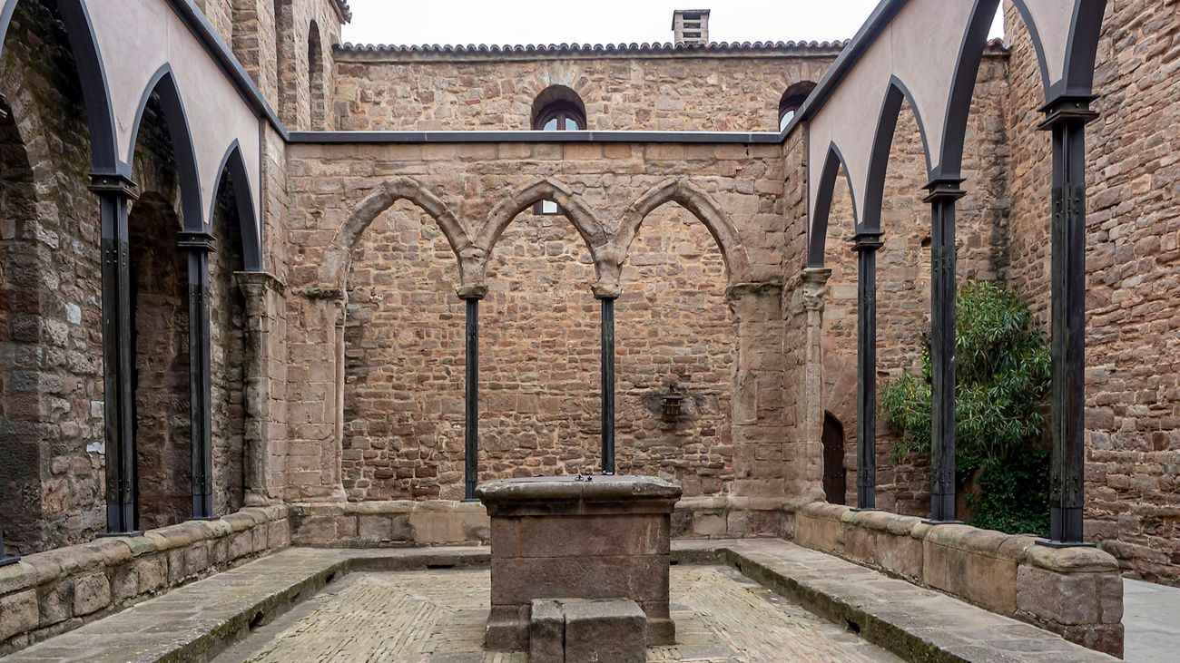 A stone cloister courtyard with pointed arches and a stone well under a pale sky