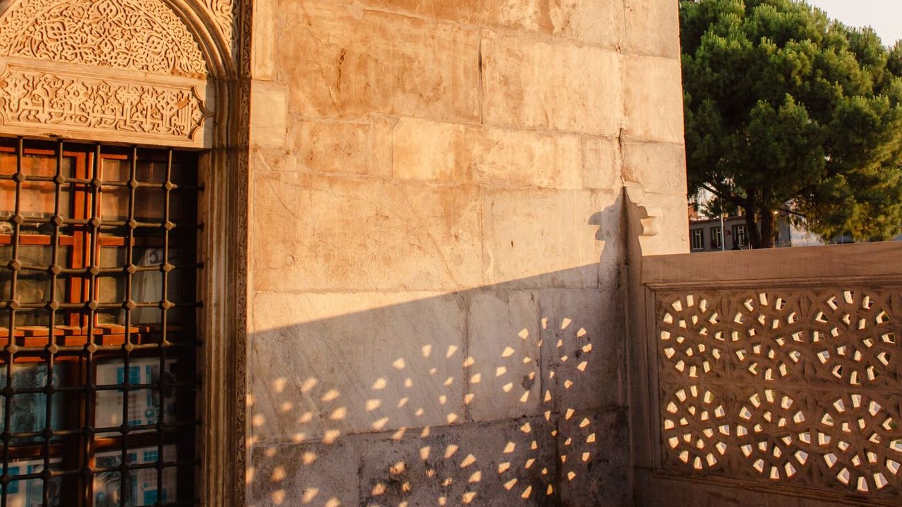 Late sun throwing patterned shadows from a carved screen onto a stone archway.